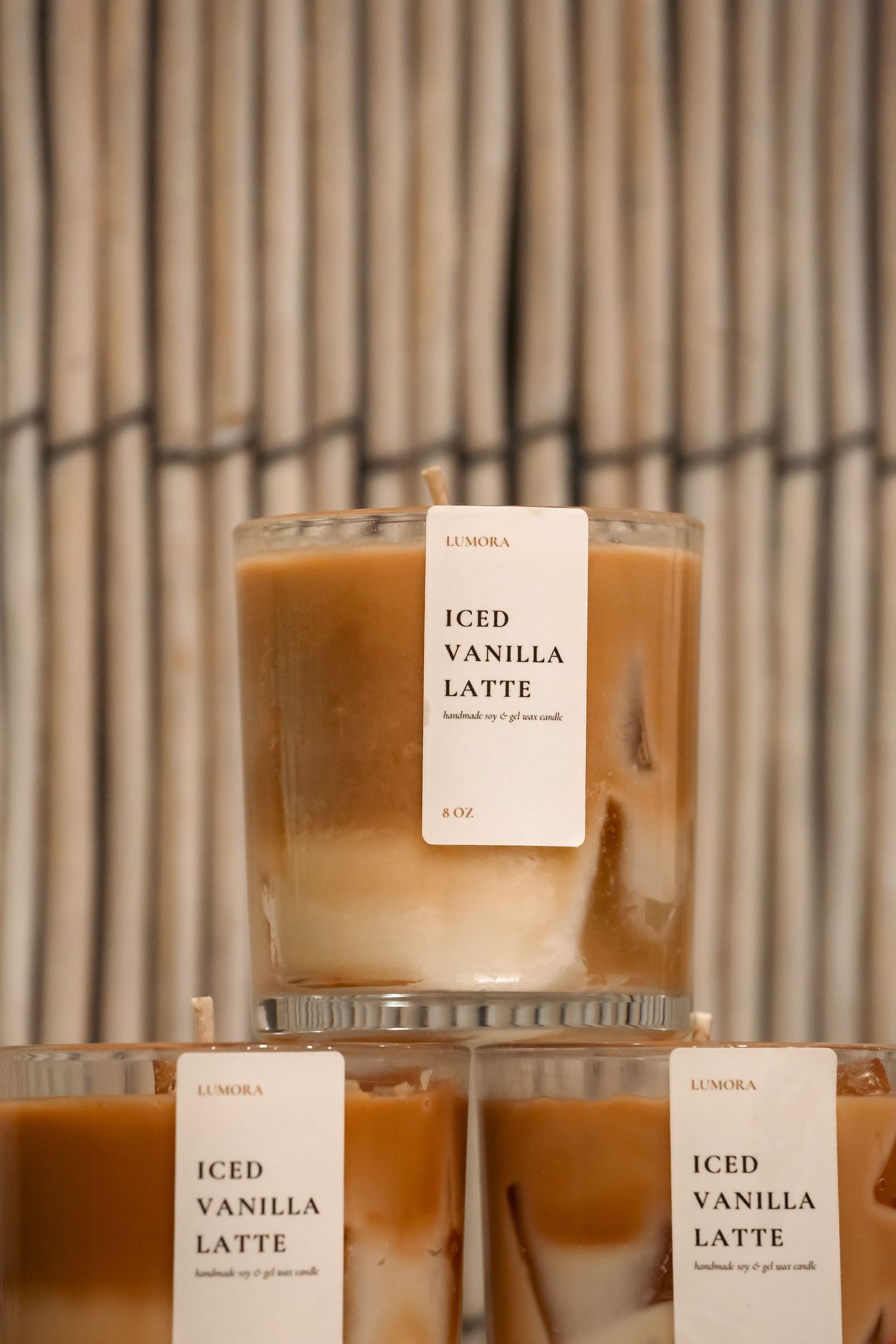 Stacked Lumora Iced Vanilla Latte scented candles in glass vessels displayed against bamboo background.