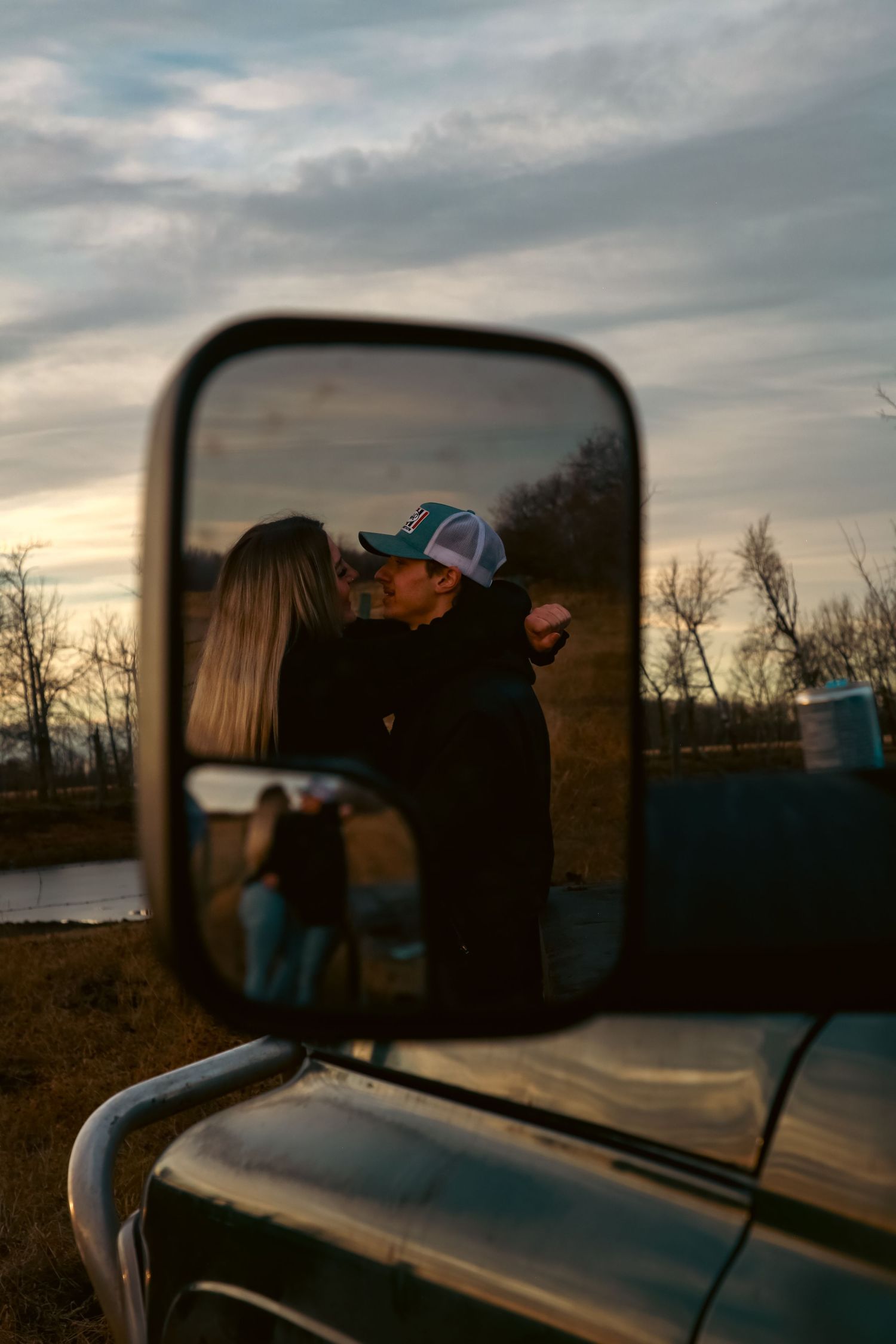 Romantic couple kissing reflected in a truck side mirror at golden hour.