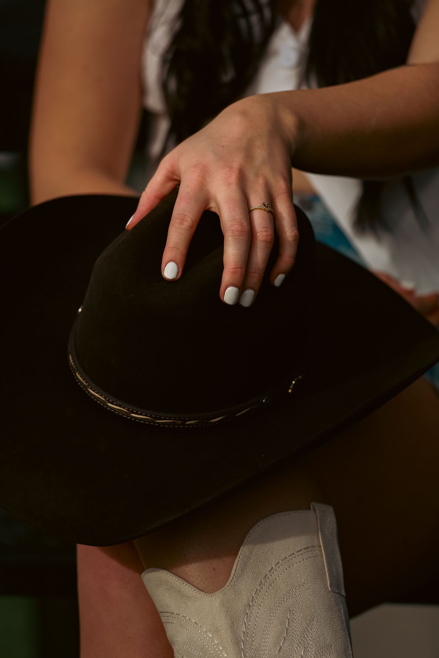 Close-up of woman's hands with white nails holding black felt cowboy hat with gold band detail.