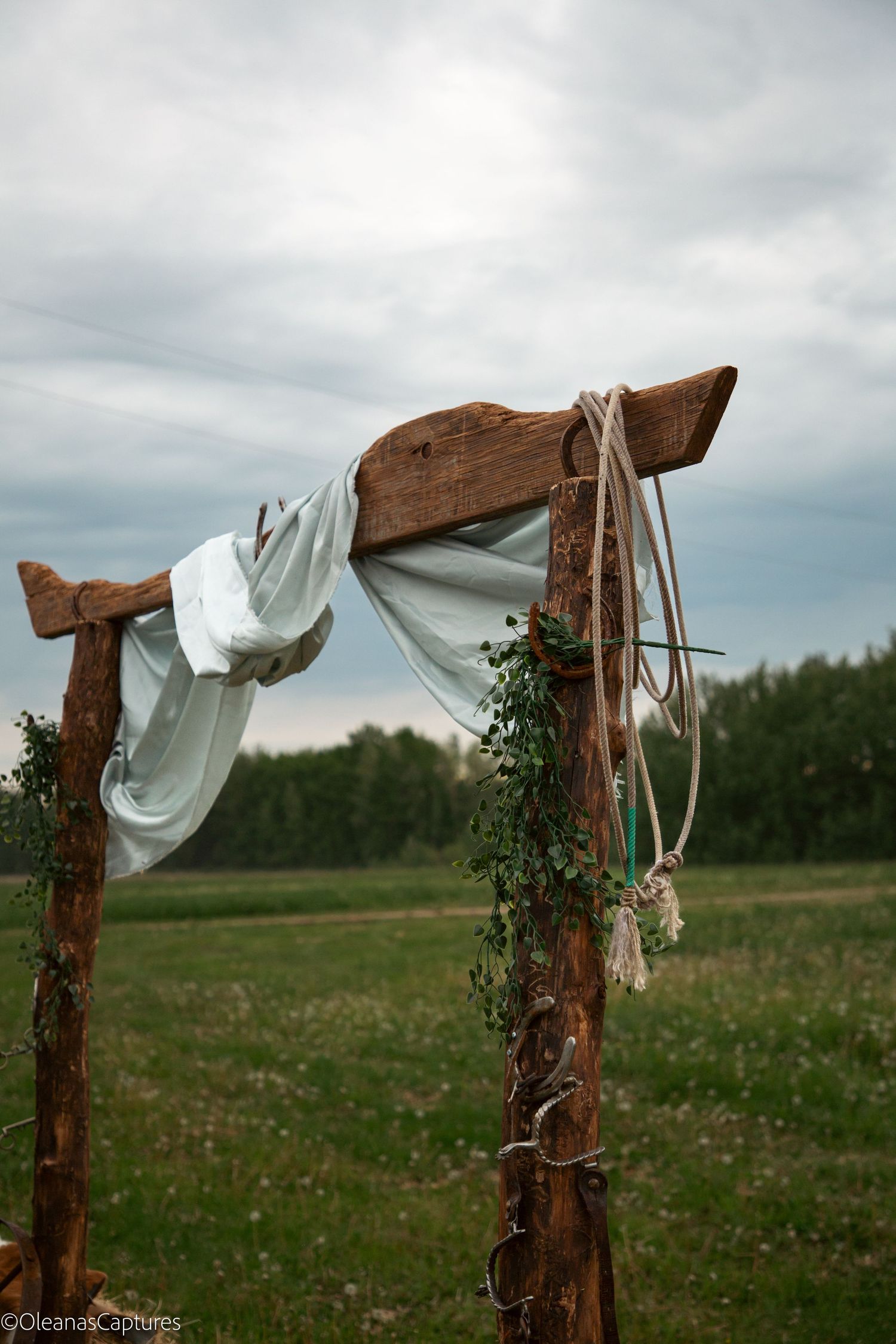 Detail of rustic wooden wedding arch corner with white draped fabric, rope lasso, and ivy greenery decoration.