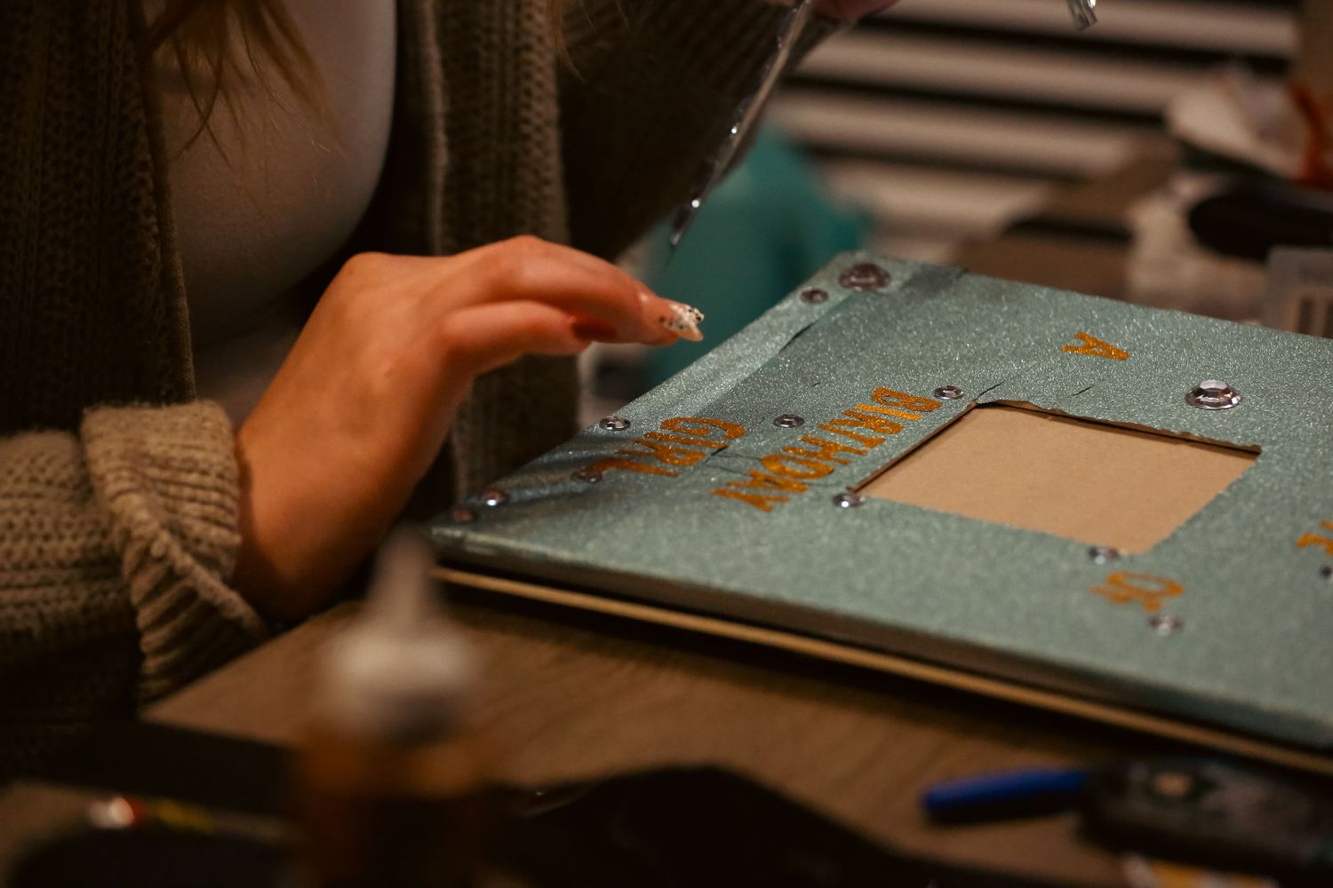 Close-up of hands working on a decorative scrapbook page with copper embellishments and rhinestones.