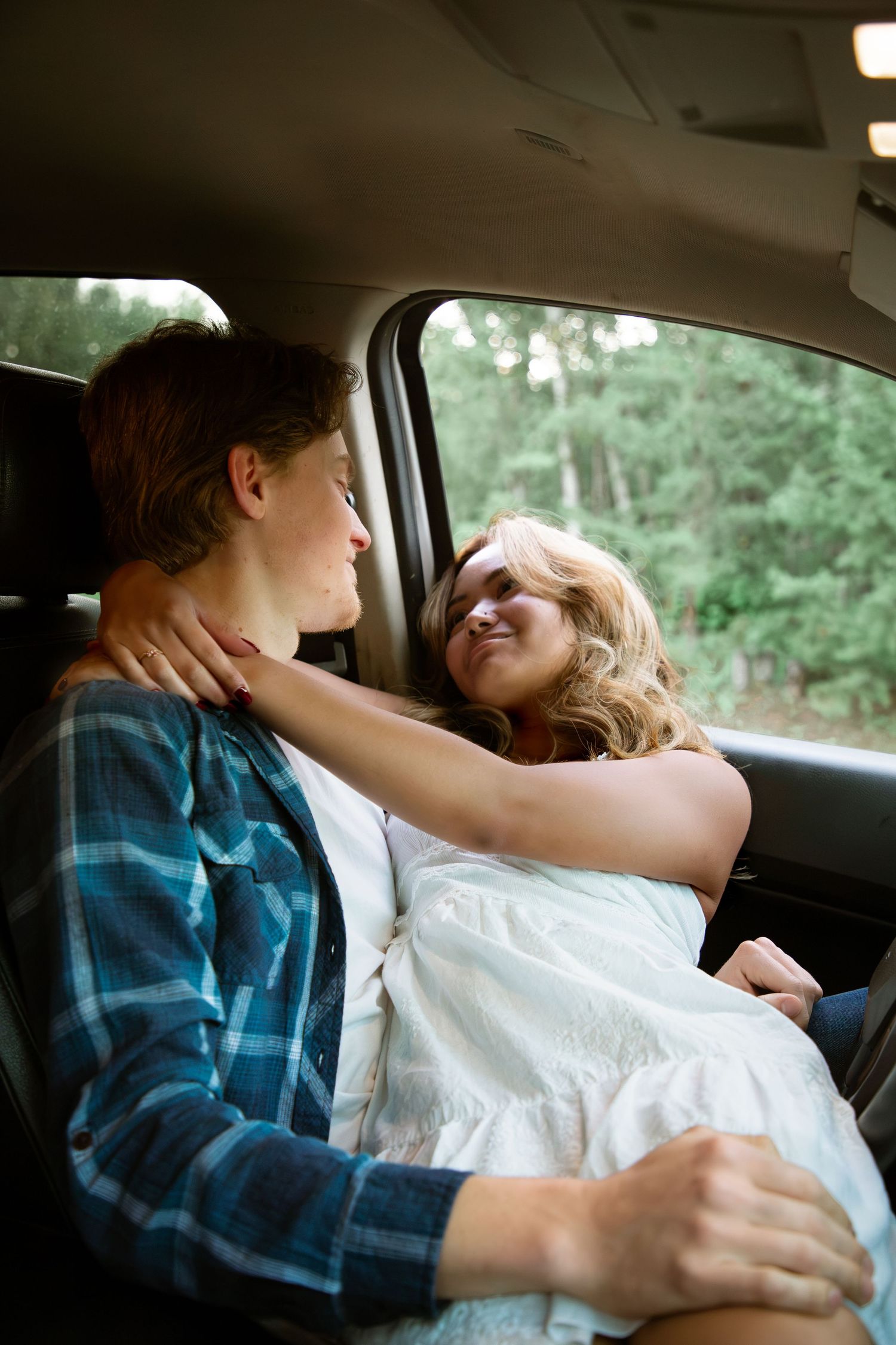 Romantic couple cuddling in the backseat of a car surrounded by lush green forest.