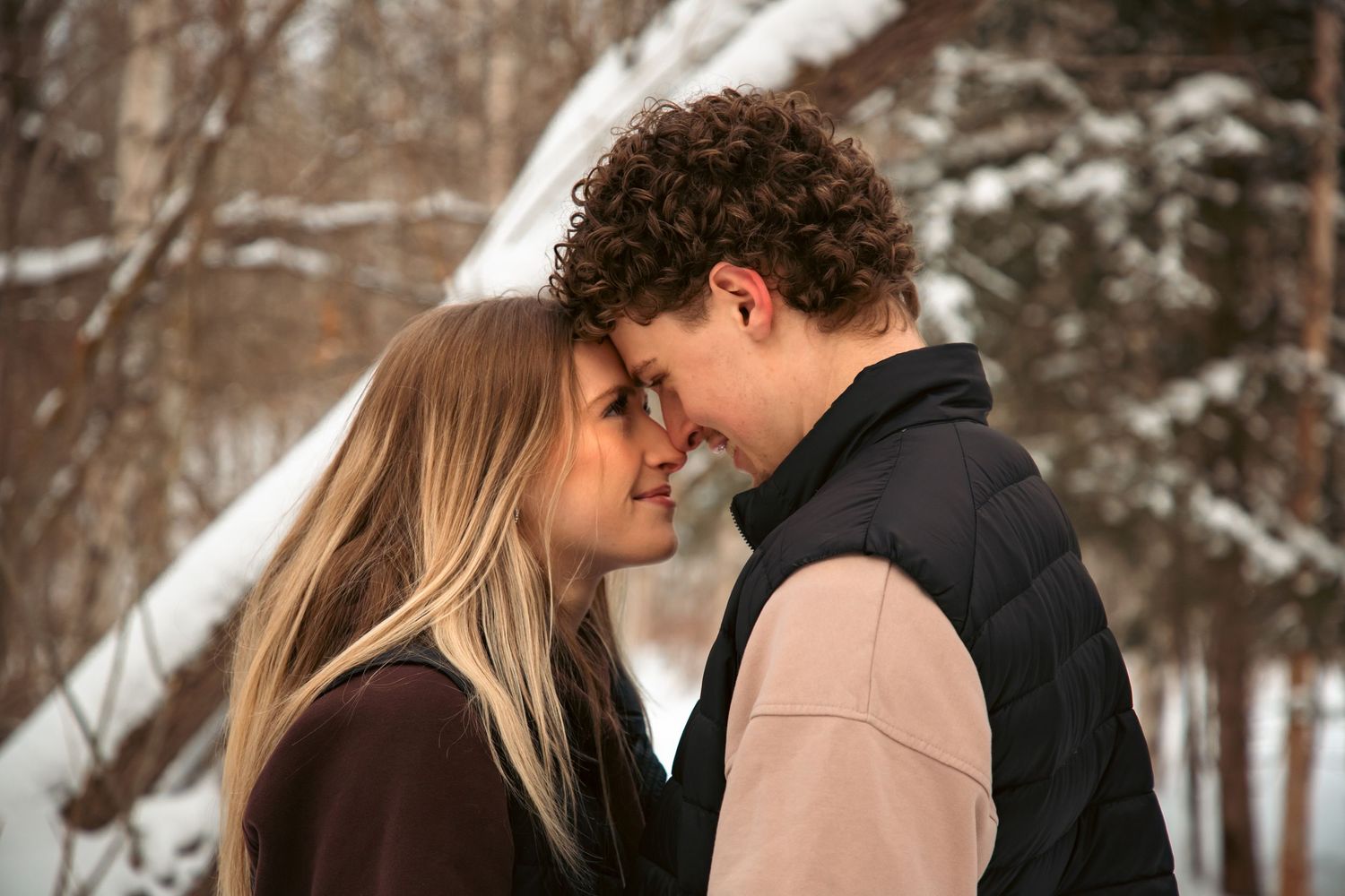 Young couple sharing a tender almost-kiss moment during a romantic winter engagement photo session.