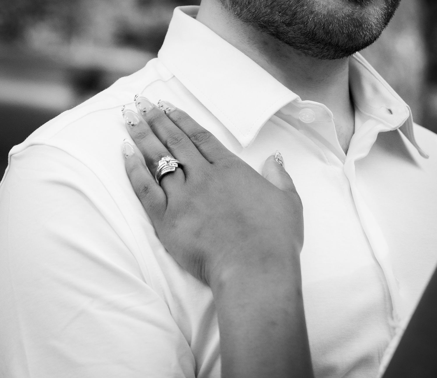 Close-up black and white photo of a bride's hand with wedding ring resting on groom's white shirt.