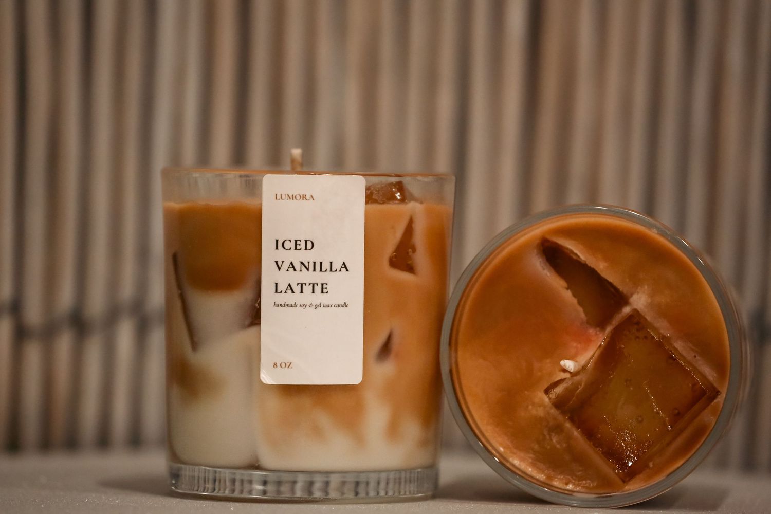 Iced vanilla latte candle by Junora displayed beside a glass of iced coffee on a bamboo background.