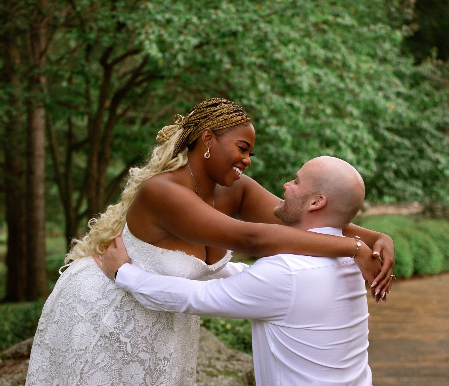 Joyful bride and groom embracing and laughing together on a tree-lined garden path.