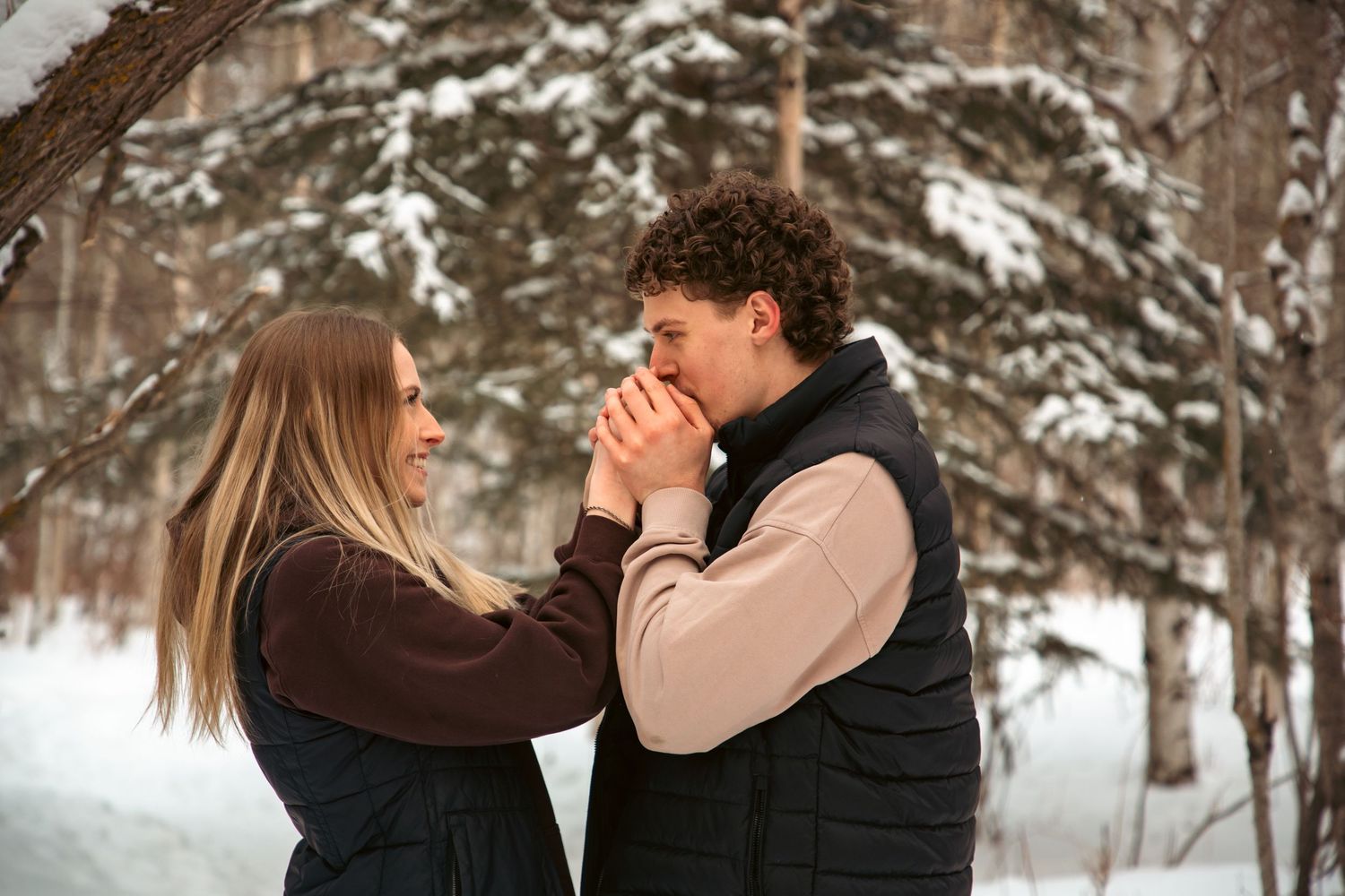 Couple holding hands together in a romantic winter forest engagement photo session in the snow.