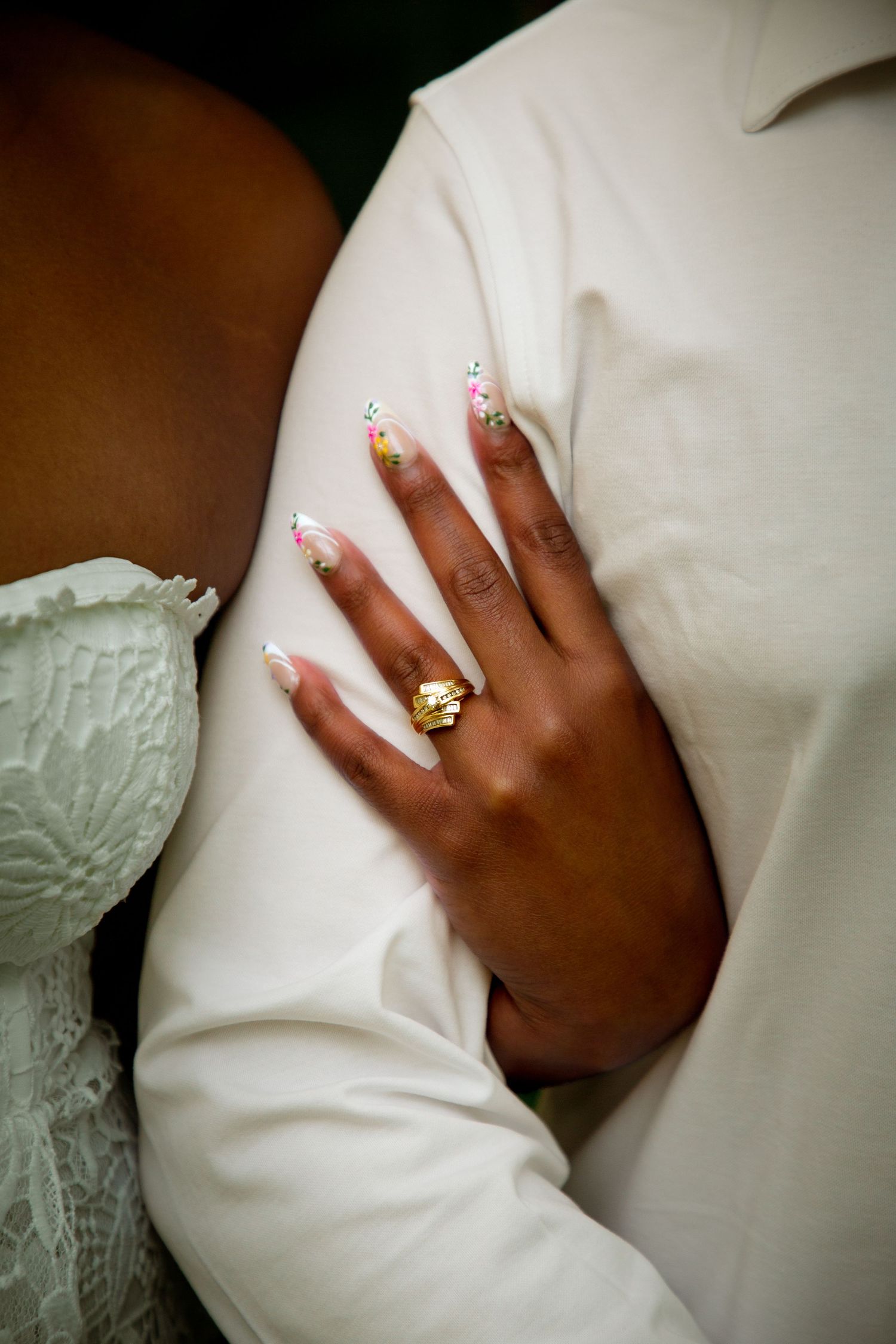 Close-up of a womans hand with floral nail art and gold ring resting on a white shirt.