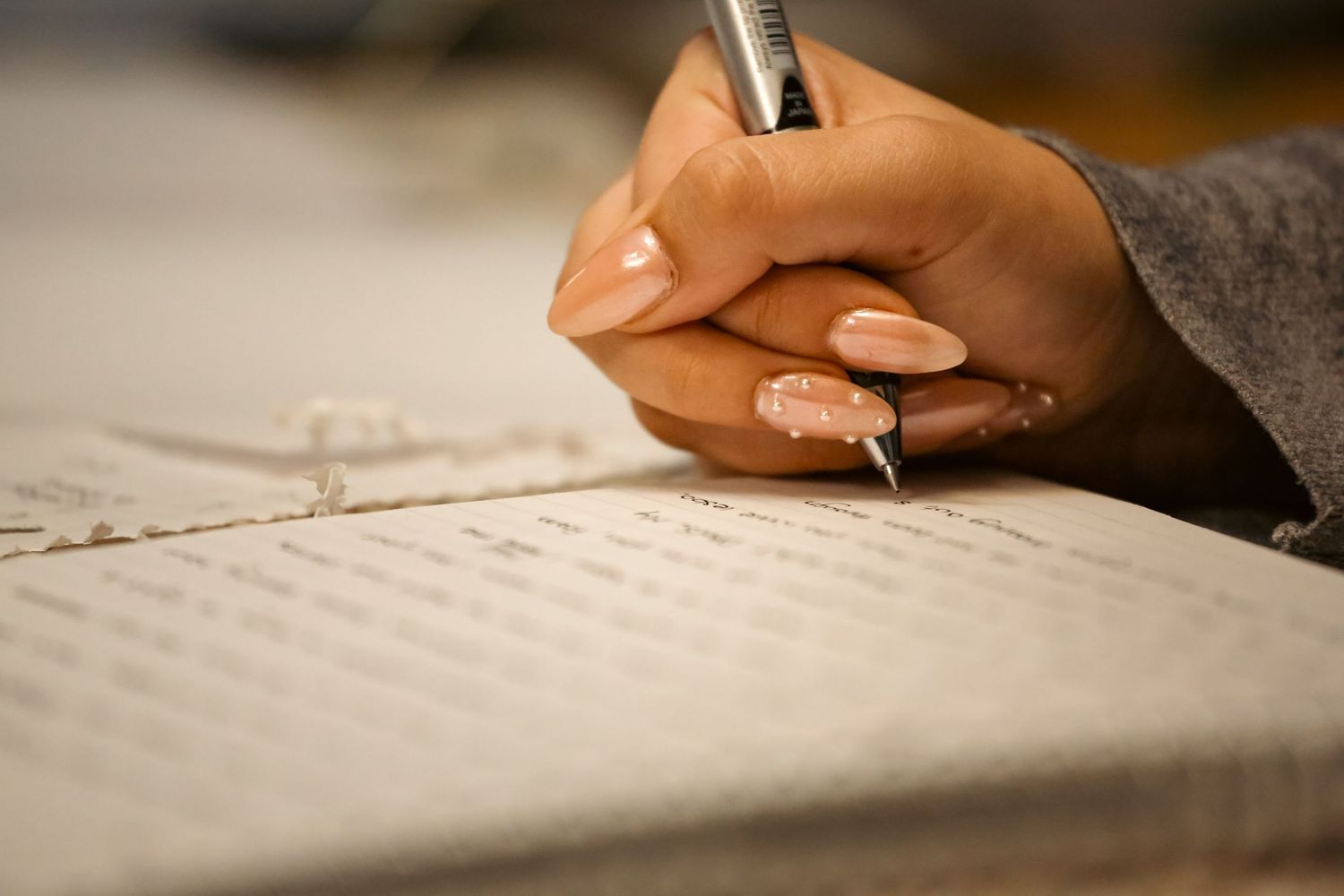 Close-up of a hand with manicured nails writing in a notebook with a silver pen.