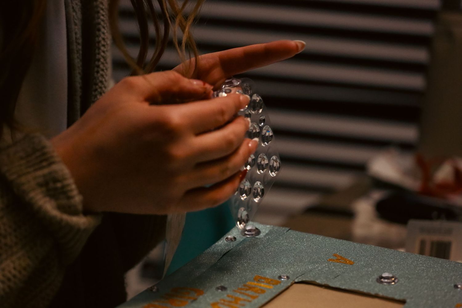 Close-up of hands carefully stringing crystal beads for handmade jewelry on a craft table.