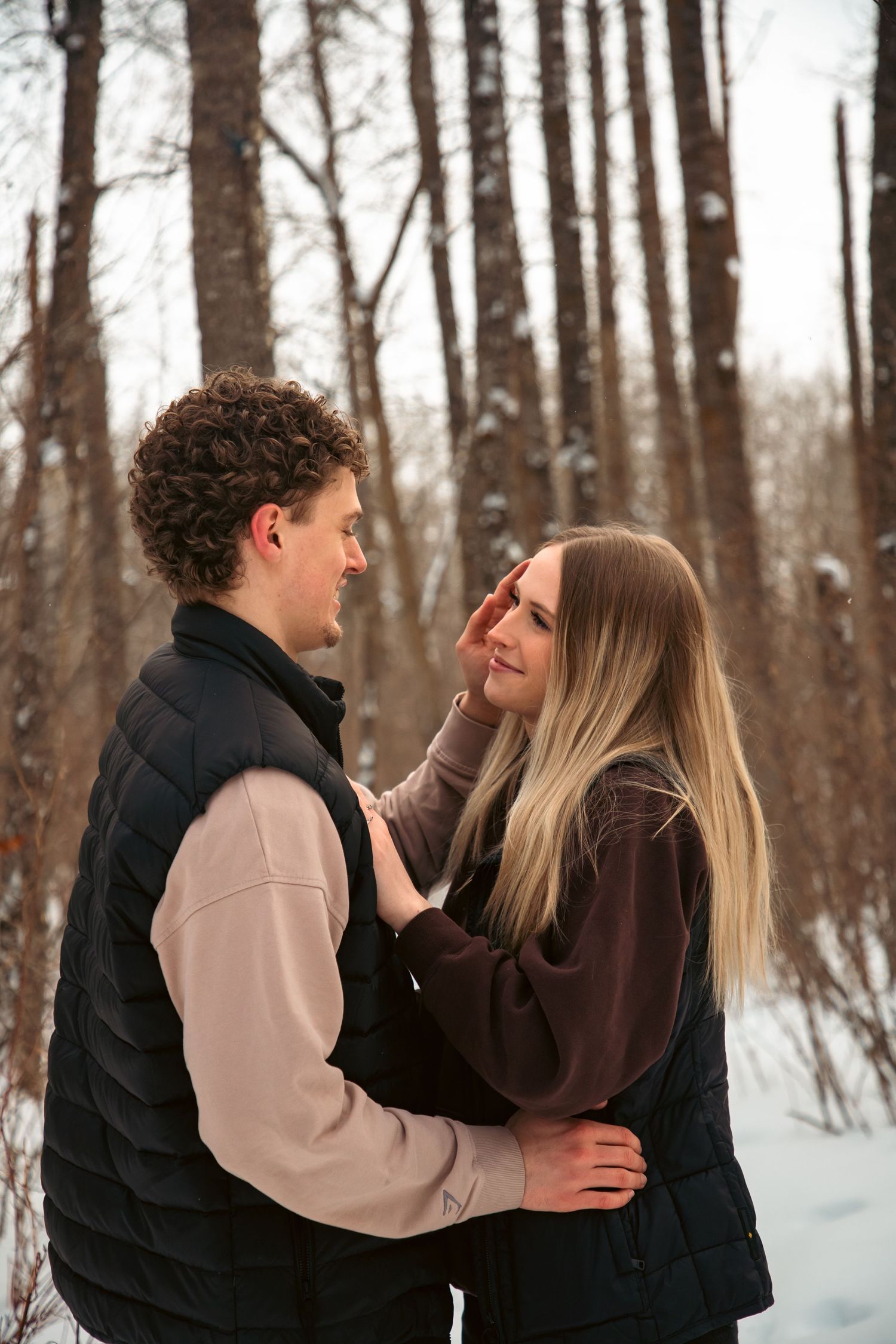 Young couple smiling and gazing lovingly at each other during a winter engagement photo session in the snow.