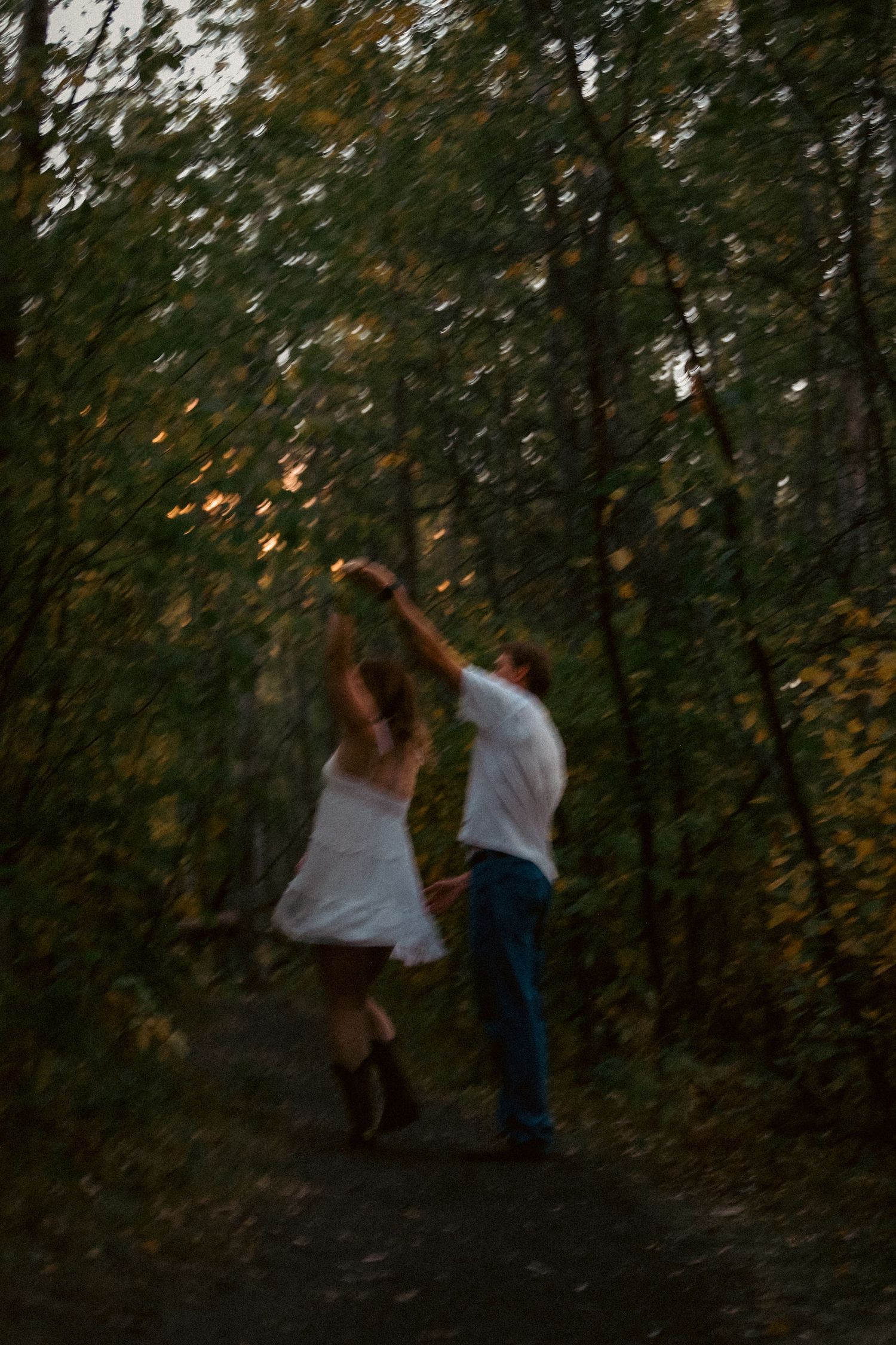 Couple dancing together on a forest path at dusk with motion blur creating a dreamy romantic effect.
