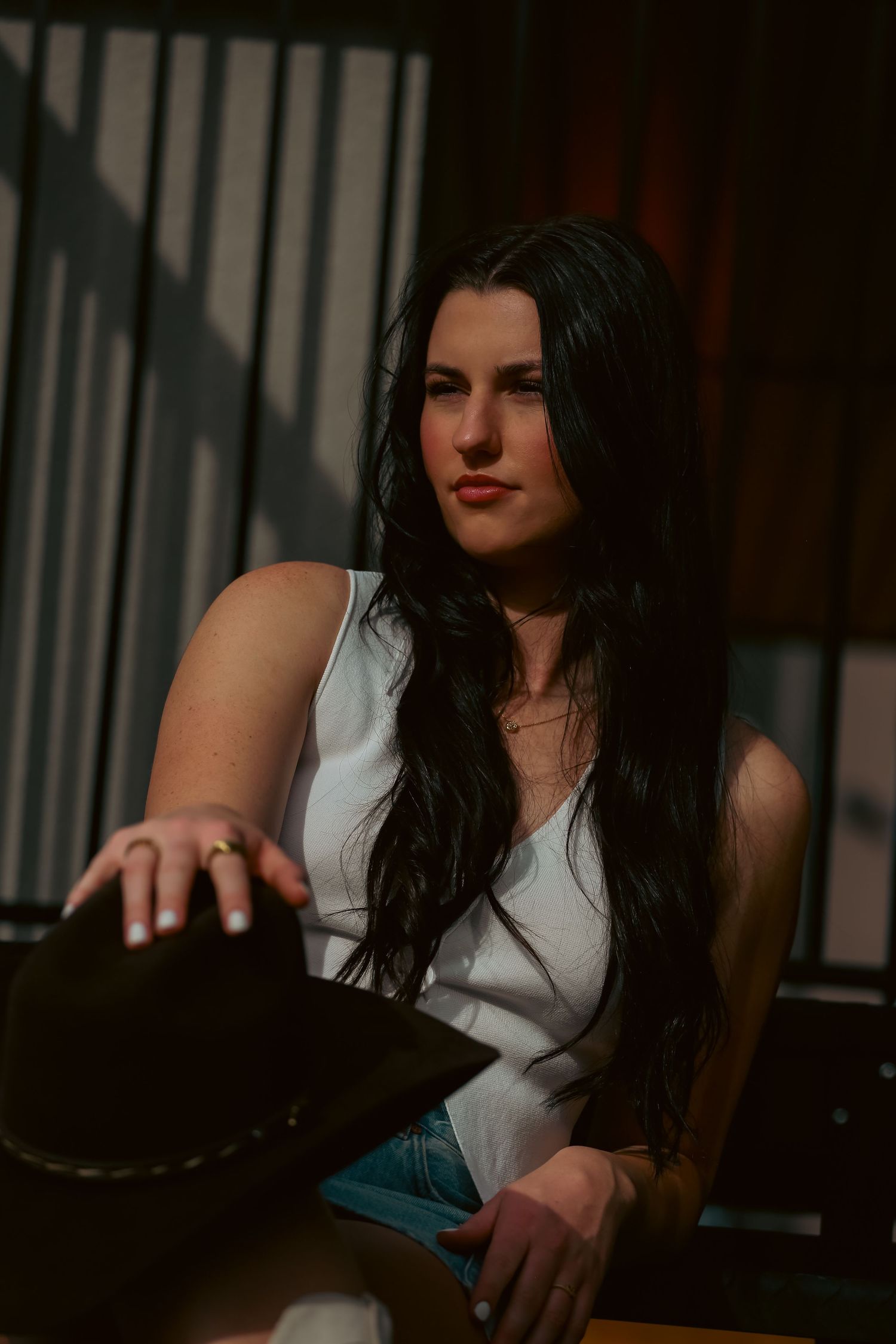 Young woman with long dark hair holding a cowboy hat in dramatic shadow lighting.