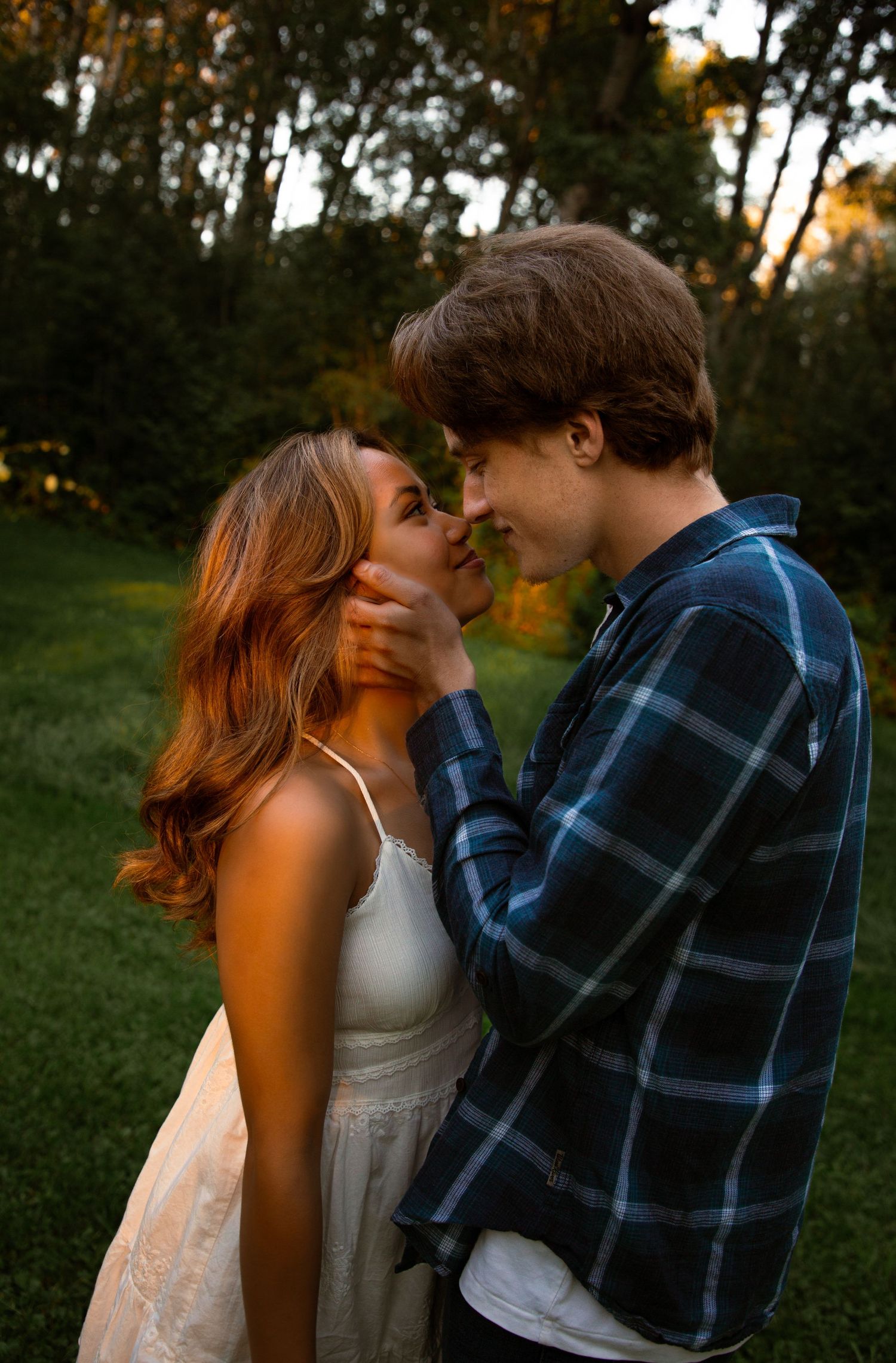 Young couple sharing a romantic almost-kiss at golden hour in a lush green outdoor setting.