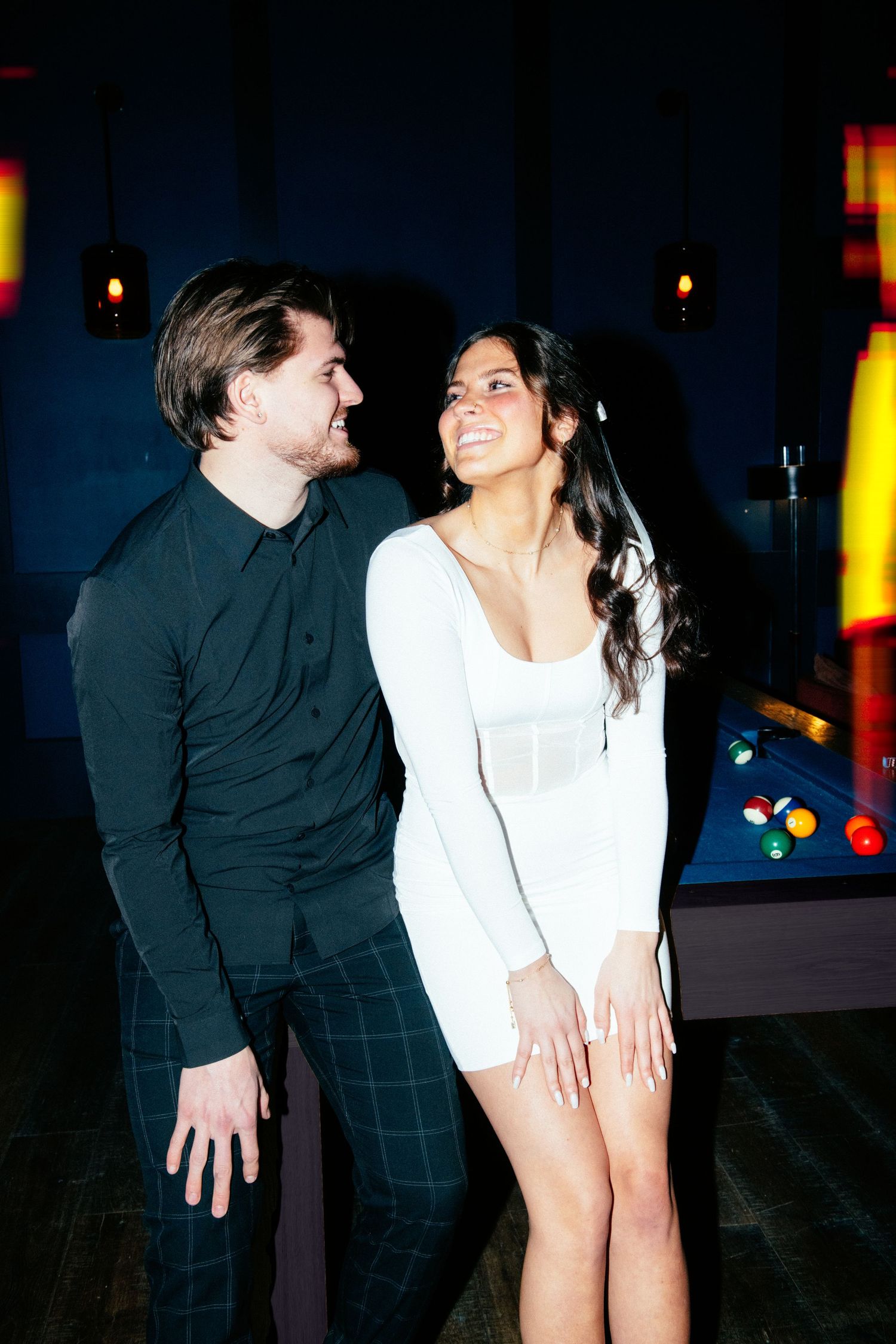 engagement photo of couple with direct flash and film light leaks sitting on a pool table
