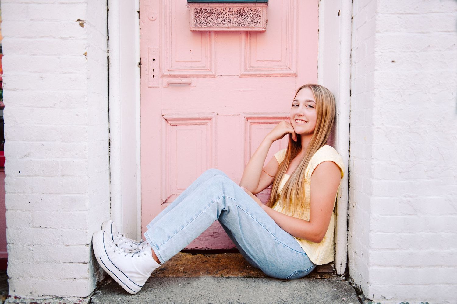 high school senior girl pictures leaning against pink door