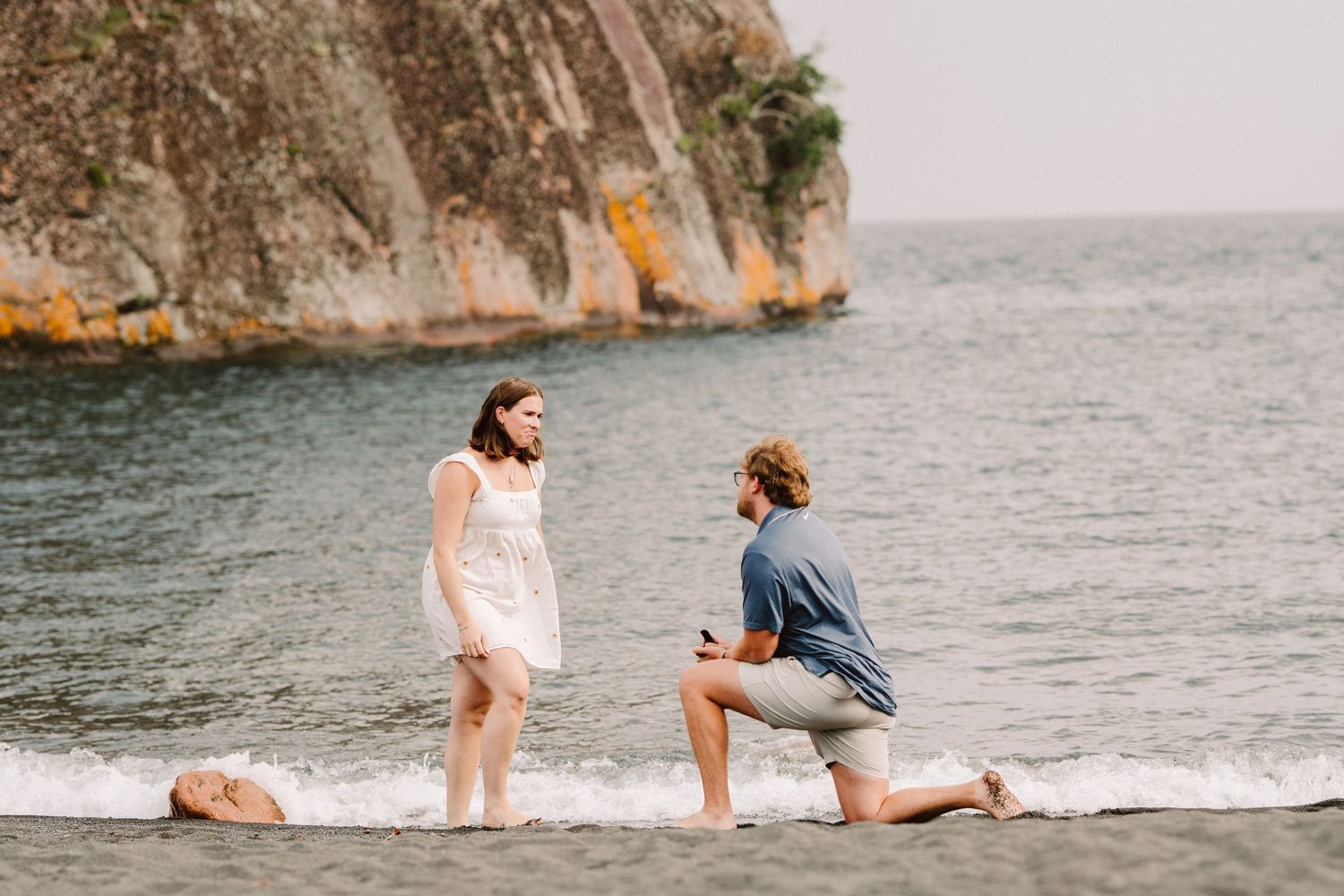 man proposing to woman on black sand beach