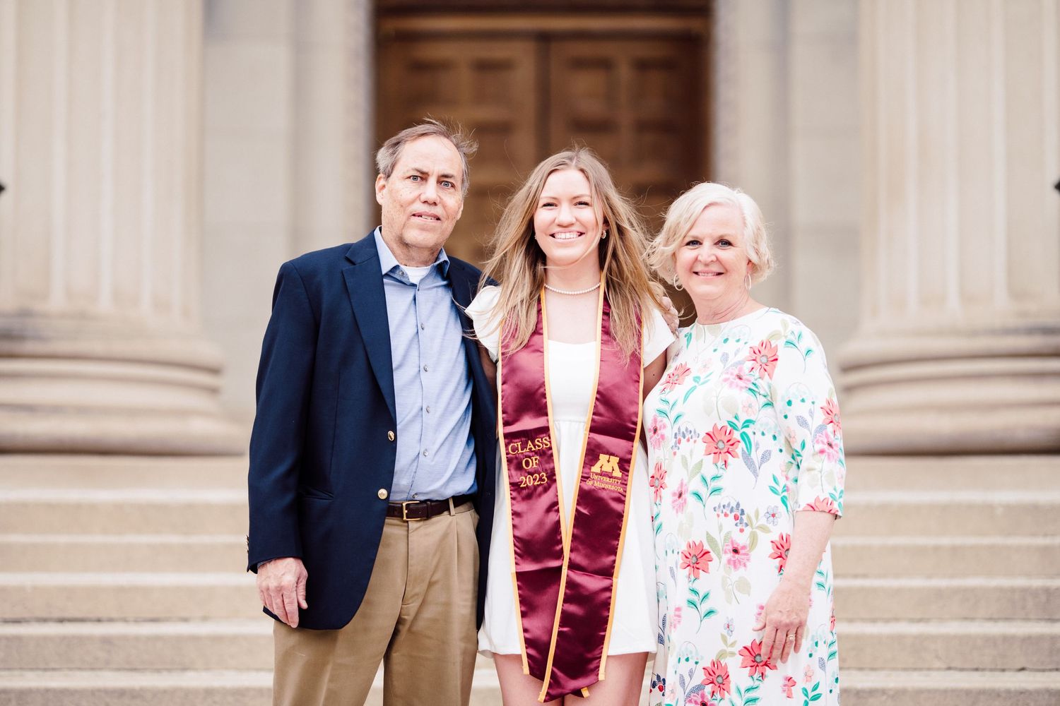 university of minnesota graduate in white dress with sash with parents