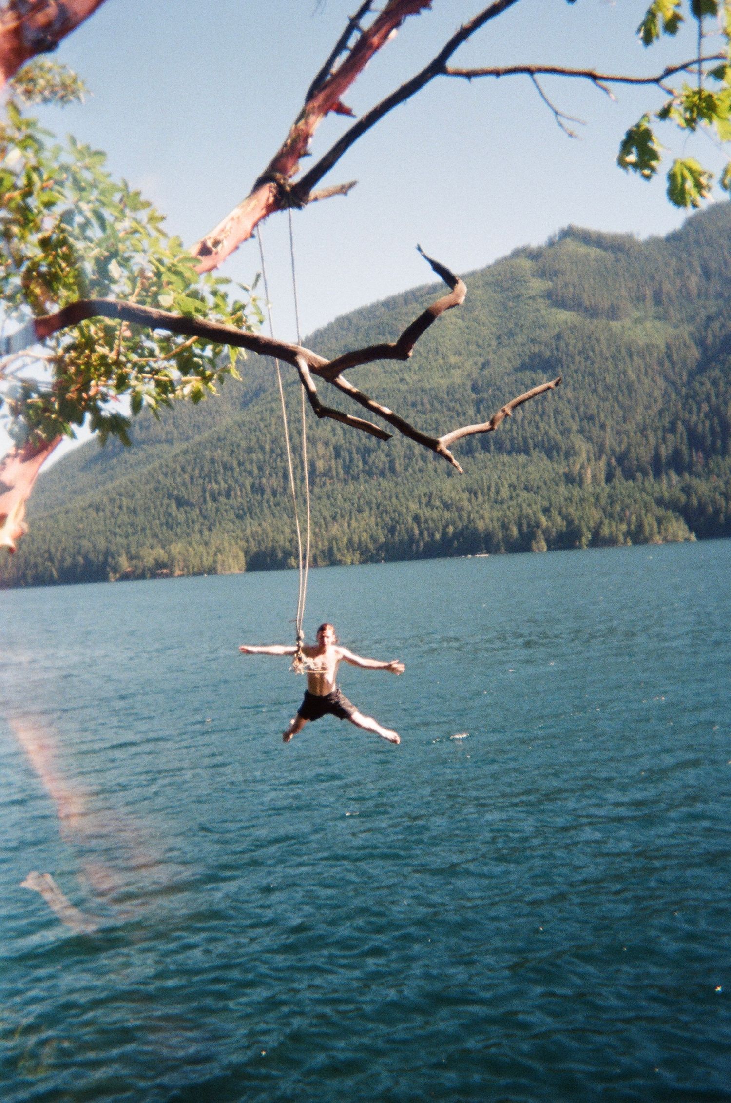 film photo of man jumping into lake off a rope swing mountain in background