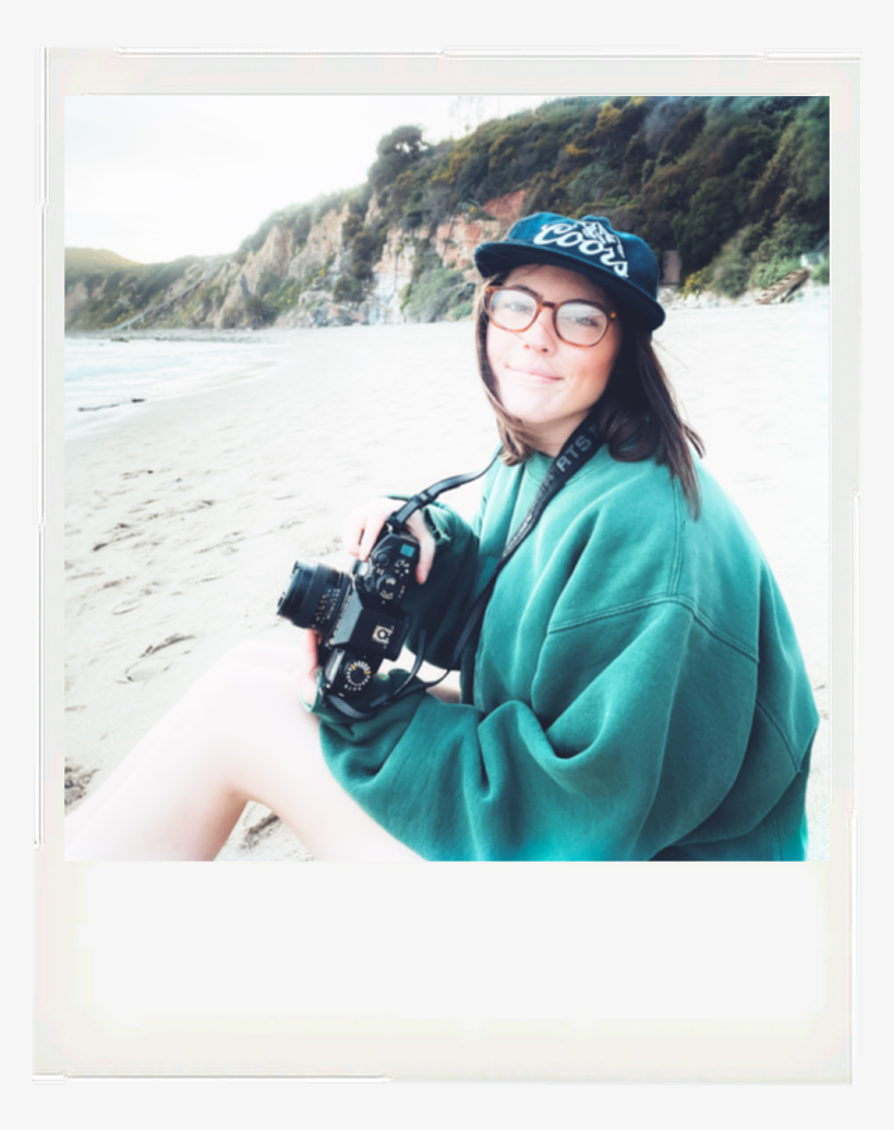 polaroid of a girl with a camera wearing a sweatshirt and hat
