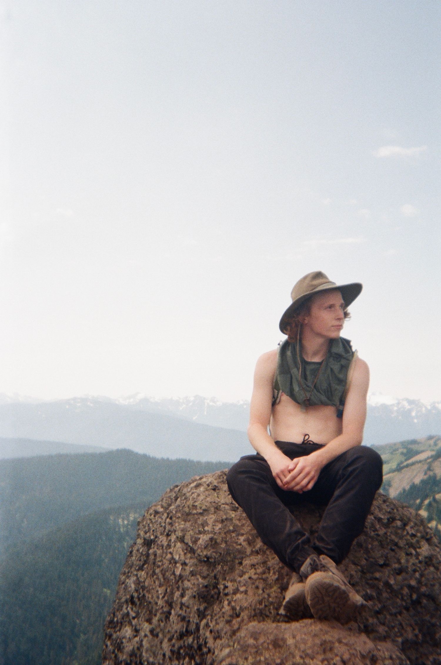 film photo of man sitting on rock on mountain