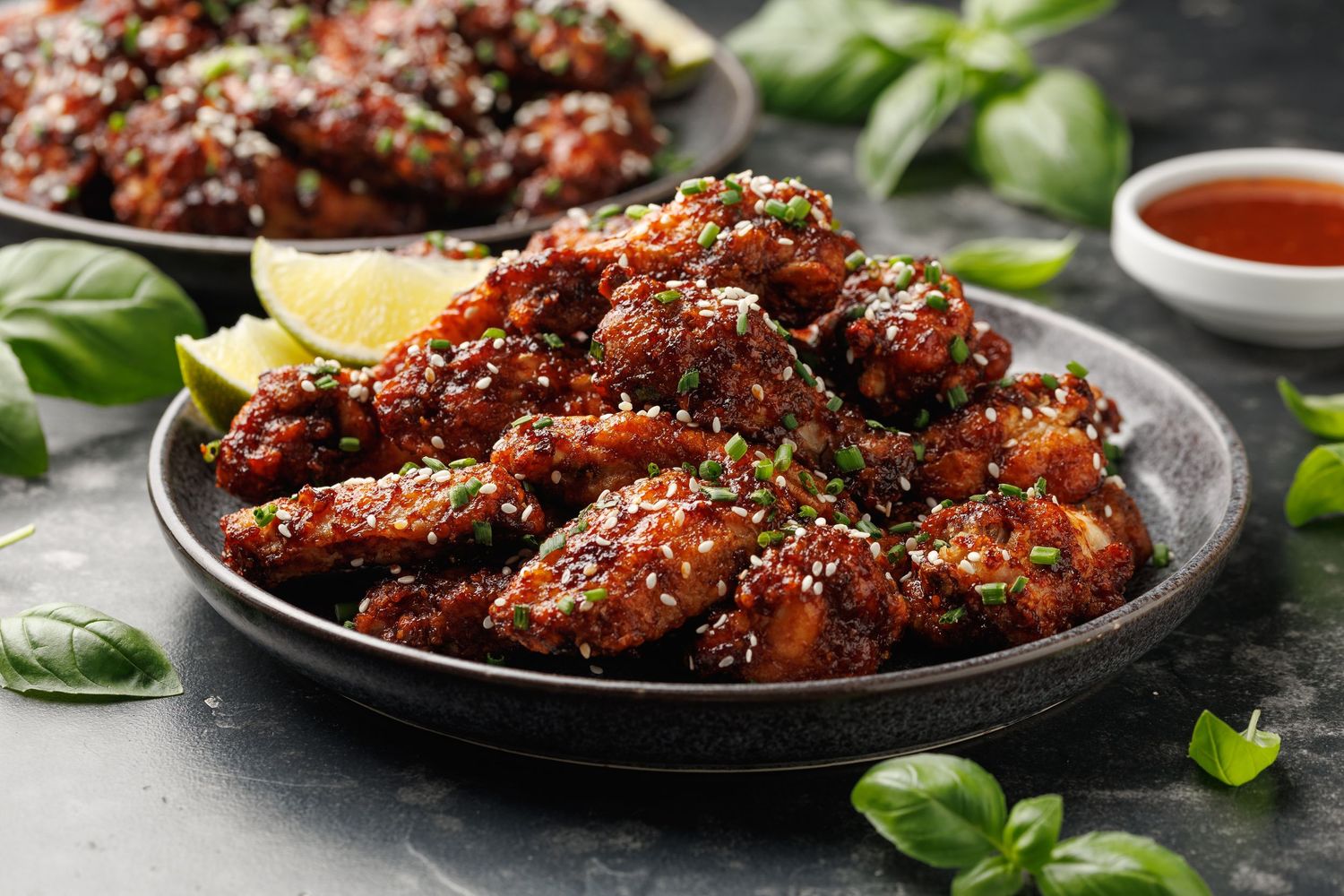 Sticky Asian glazed chicken wings garnished with sesame seeds and green herbs on dark plates.