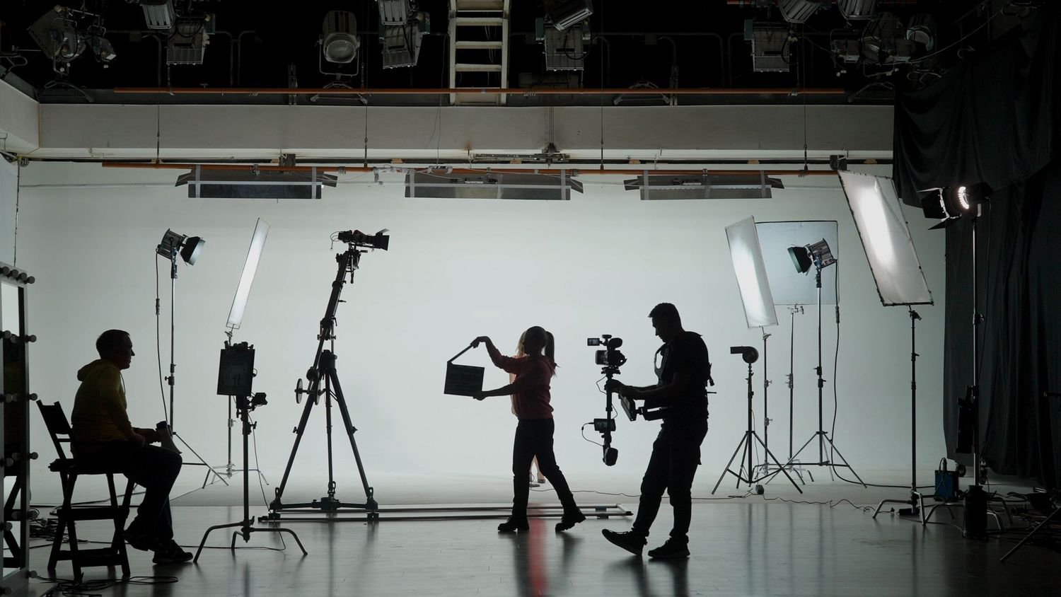 A panoramic view of a photography studio setup with lighting equipment, cameras, and silhouettes of people working.