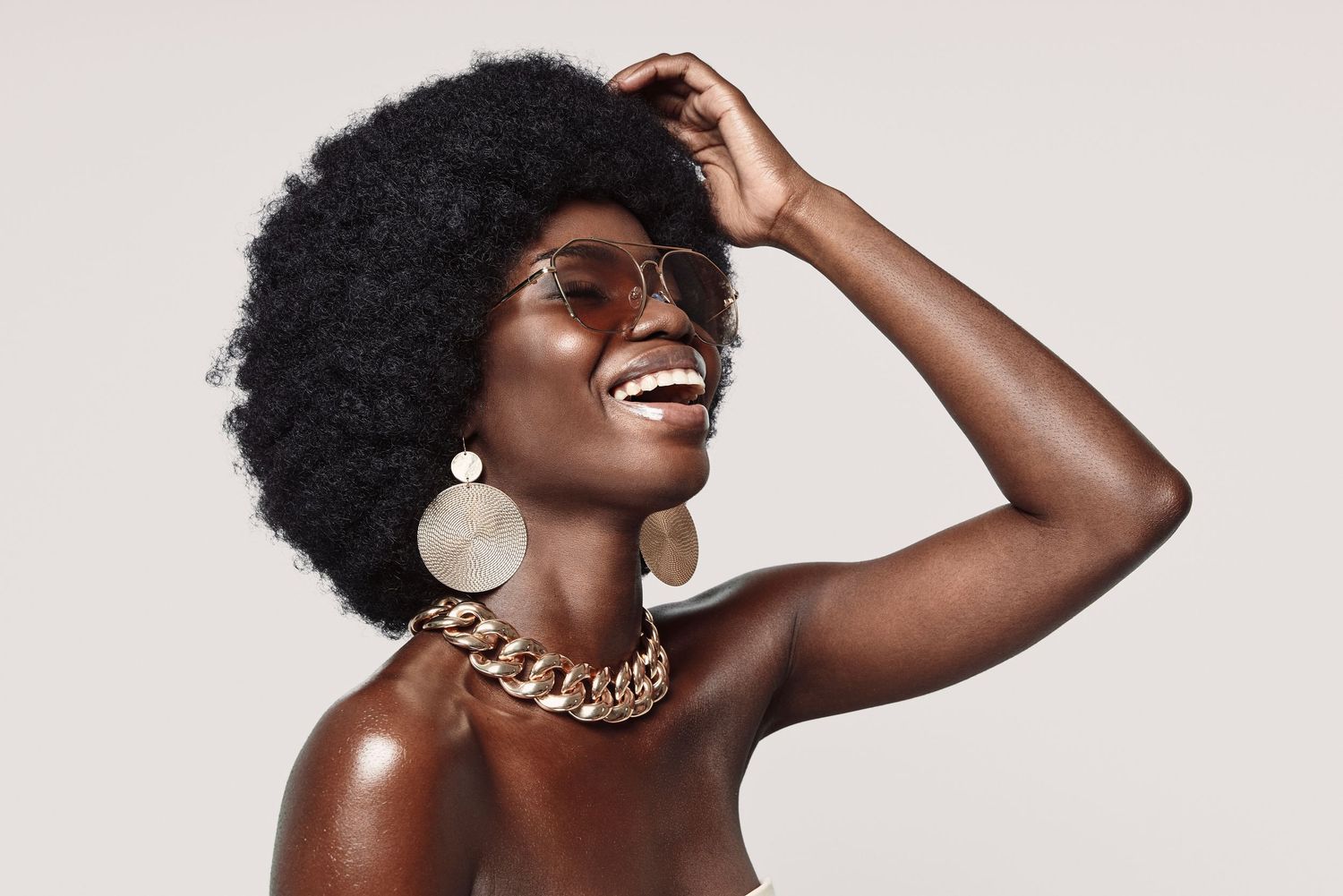 Person wearing gold jewelry and white hoop earrings laughs joyfully against a light background.