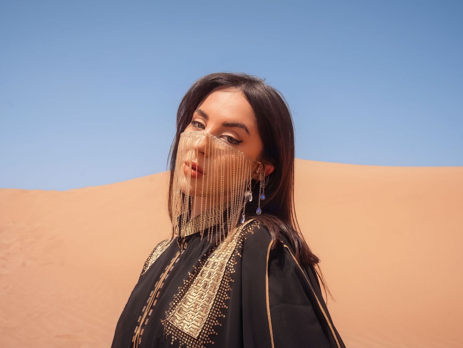 A dramatic desert portrait with flowing hair against sand dunes and blue sky.