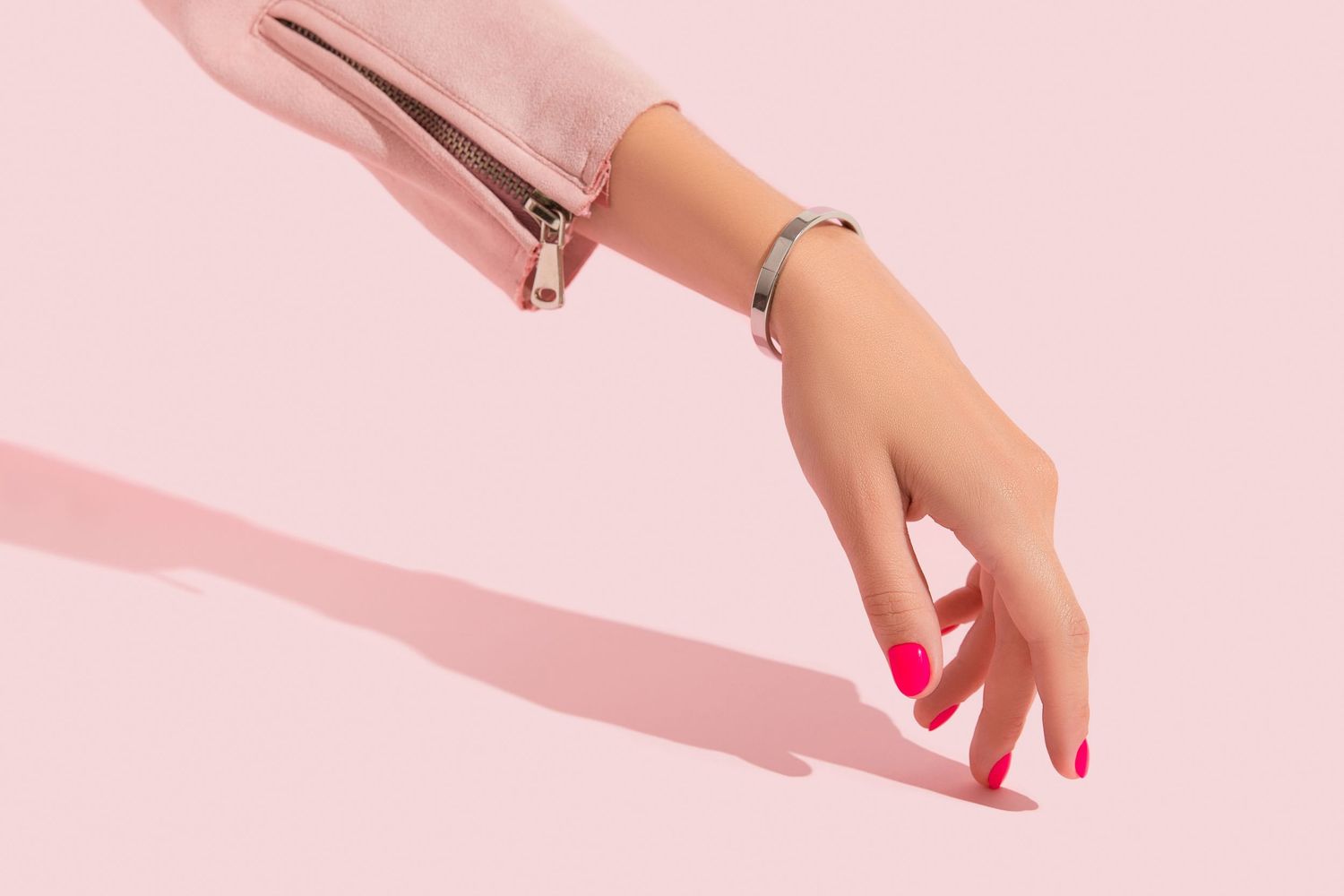 Hand with bright pink manicure holds a pink beauty product against a soft pink background.