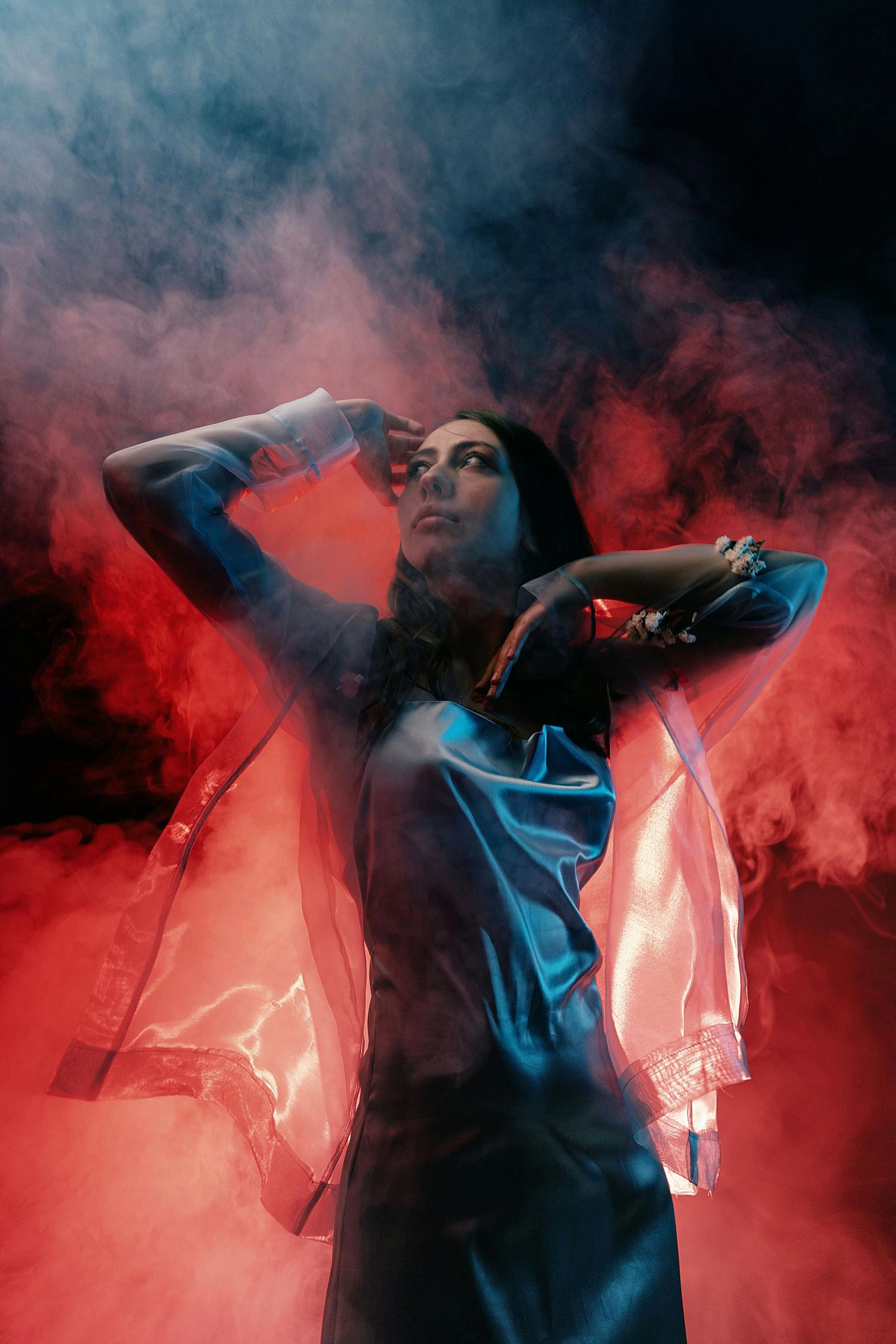 A silhouetted figure poses dramatically against a backdrop of red and blue smoke creating an atmospheric dance scene.