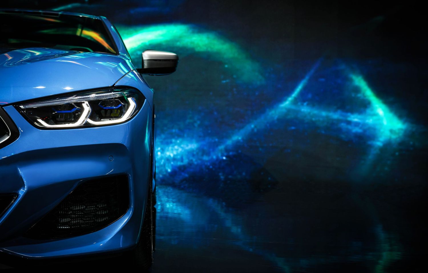 Close-up view of modern BMW car headlights and grille details illuminated in dramatic blue lighting.