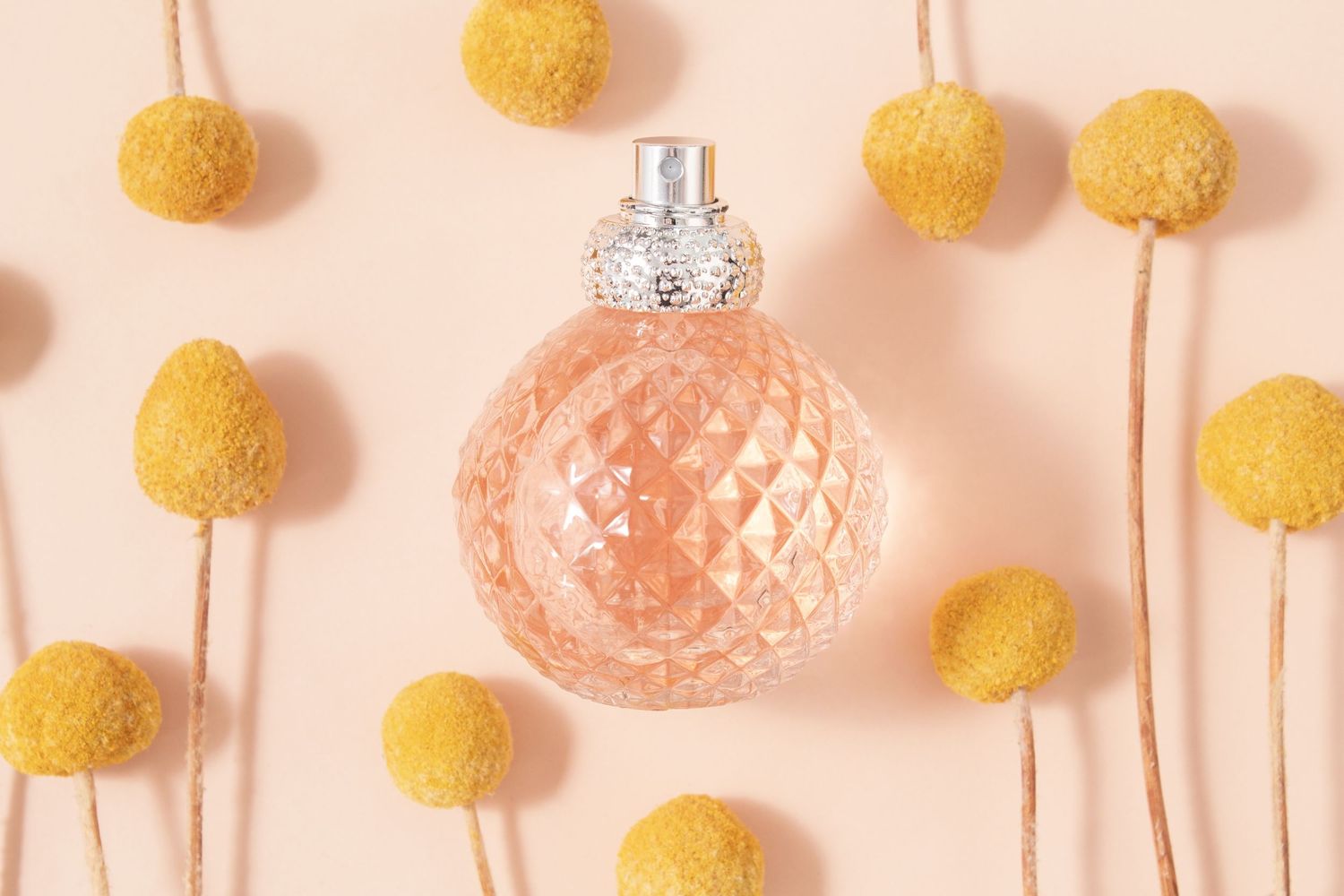 Pink glass Christmas ornaments and yellow pom pom decorations arranged on a pastel peach background.