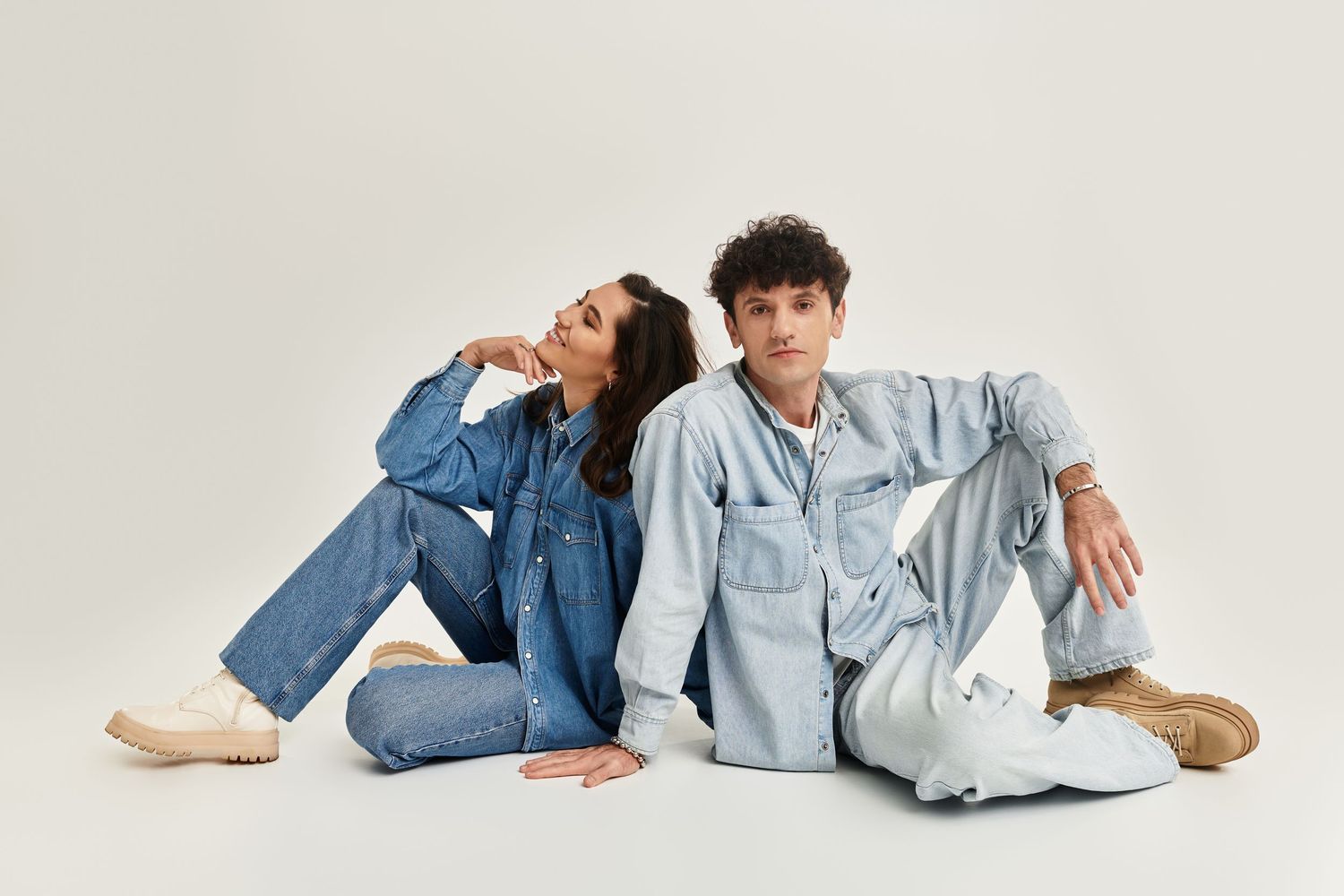 People in casual denim and chambray outfits lying down in relaxed poses against white background.