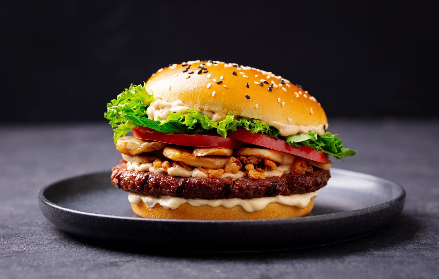 Juicy cheeseburger with melted cheese, lettuce, and tomato on a sesame seed bun against a dark background.