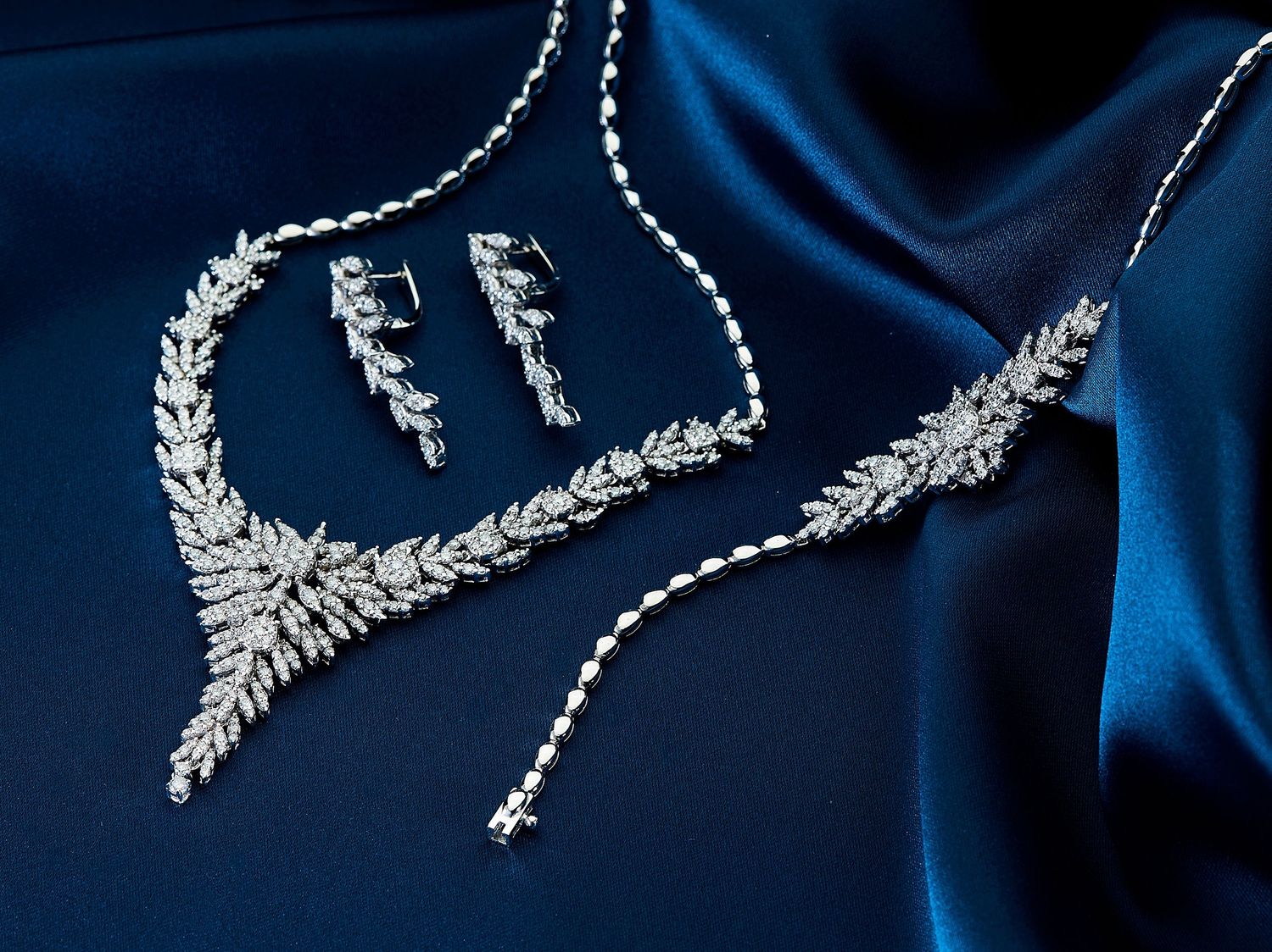 Elegant crystal bridal necklace and earring set with floral motifs sparkles against a dark blue background.