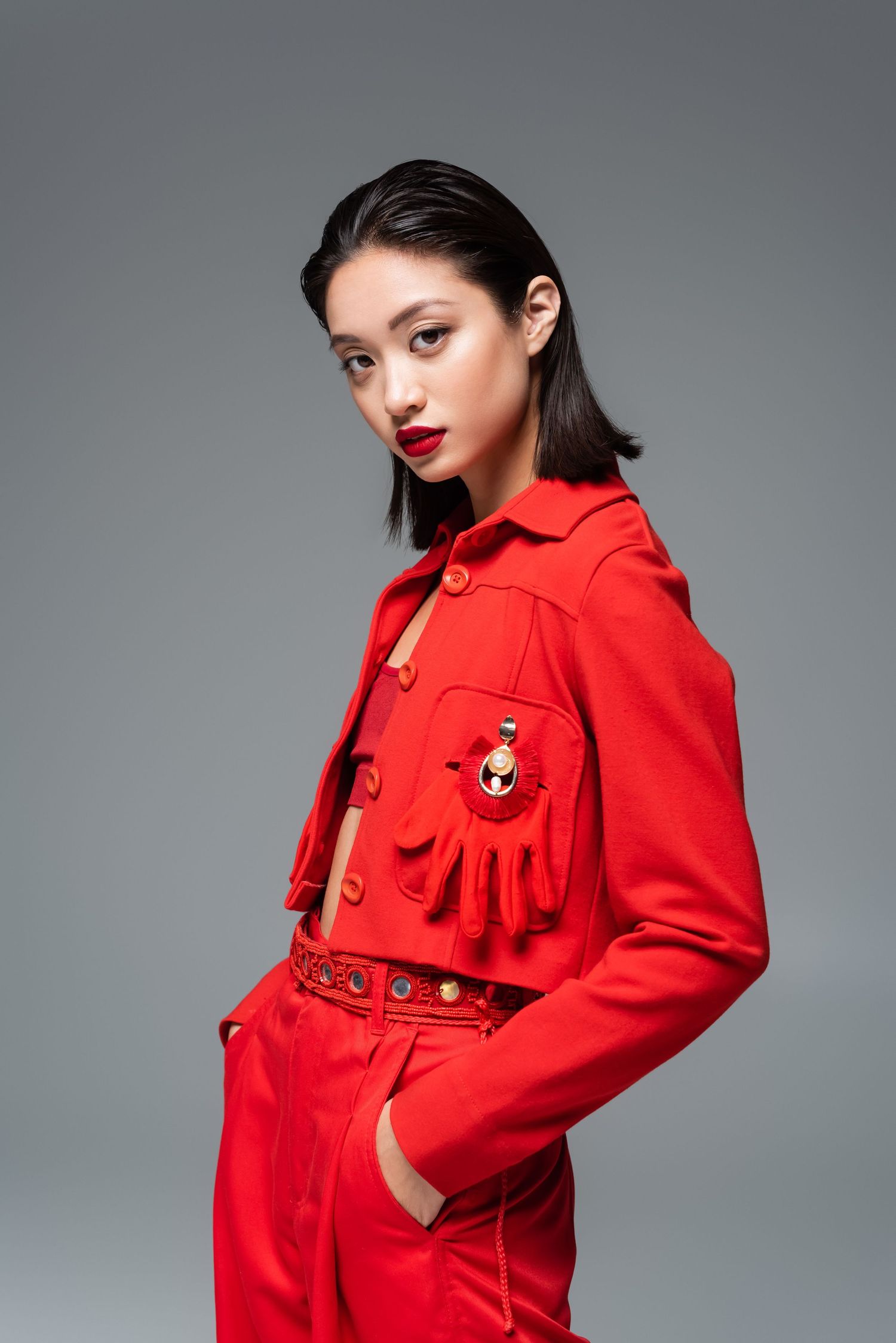 Fashion model wearing a vibrant red coat with statement buttons poses against a gray studio backdrop.