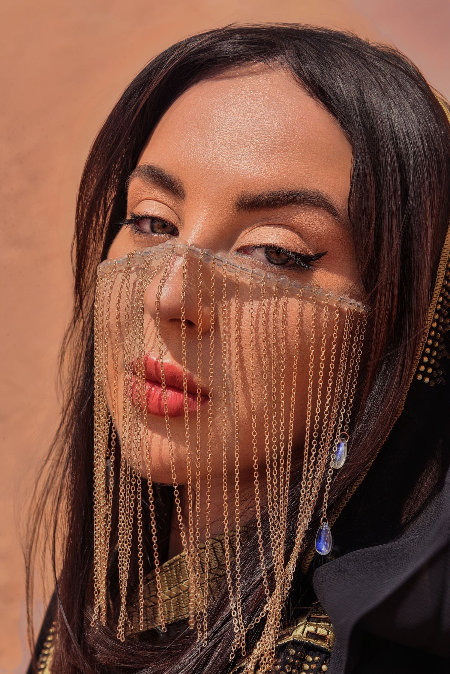 Close-up shot showing gold chain veil detail against desert background.