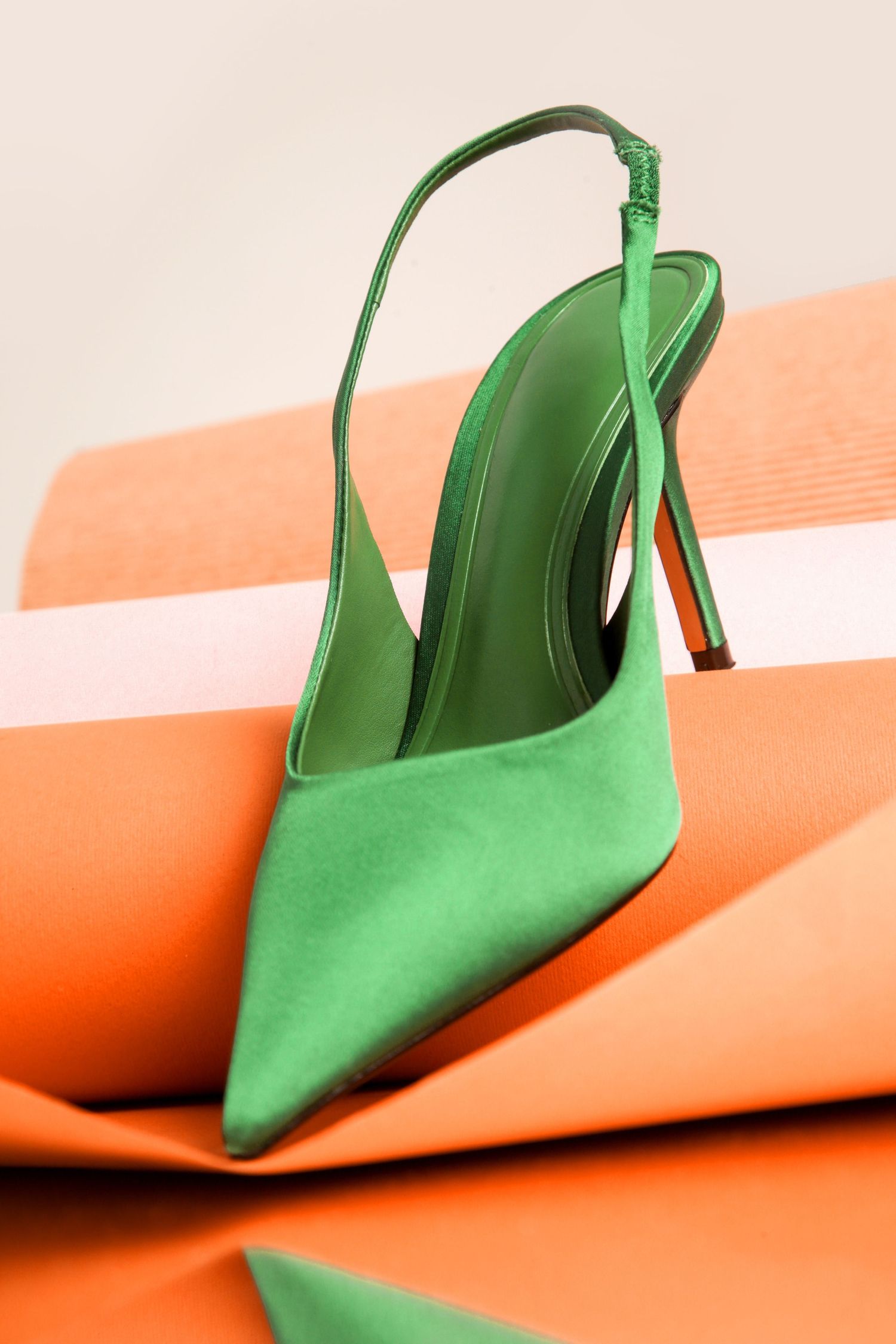 Green suede slingback kitten heel shoe positioned against orange and white diagonal striped background.