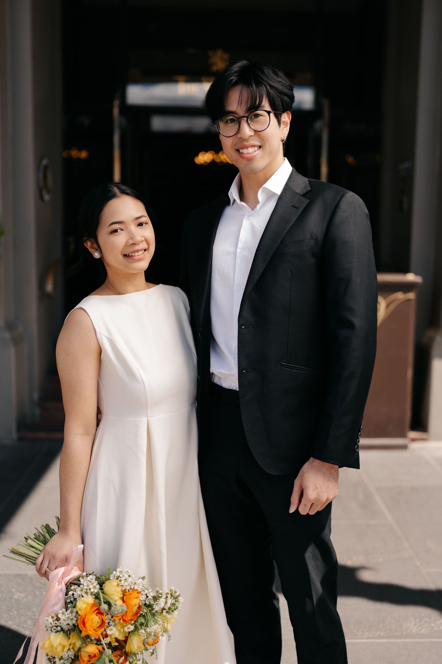 Newlyweds share candid moments together while holding vibrant orange and yellow floral bouquet.