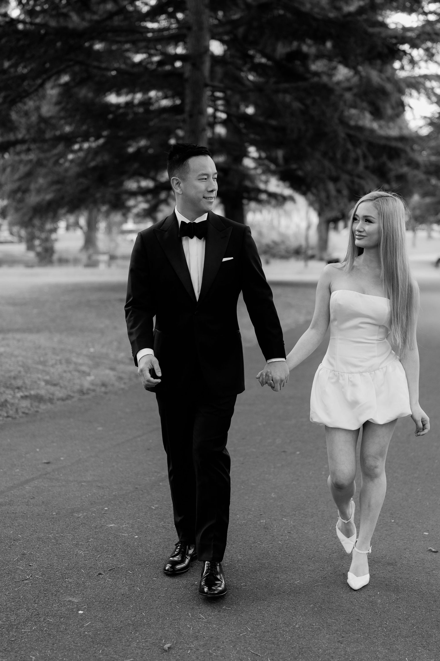 A couple in black and white formal wear walks together on a garden path.