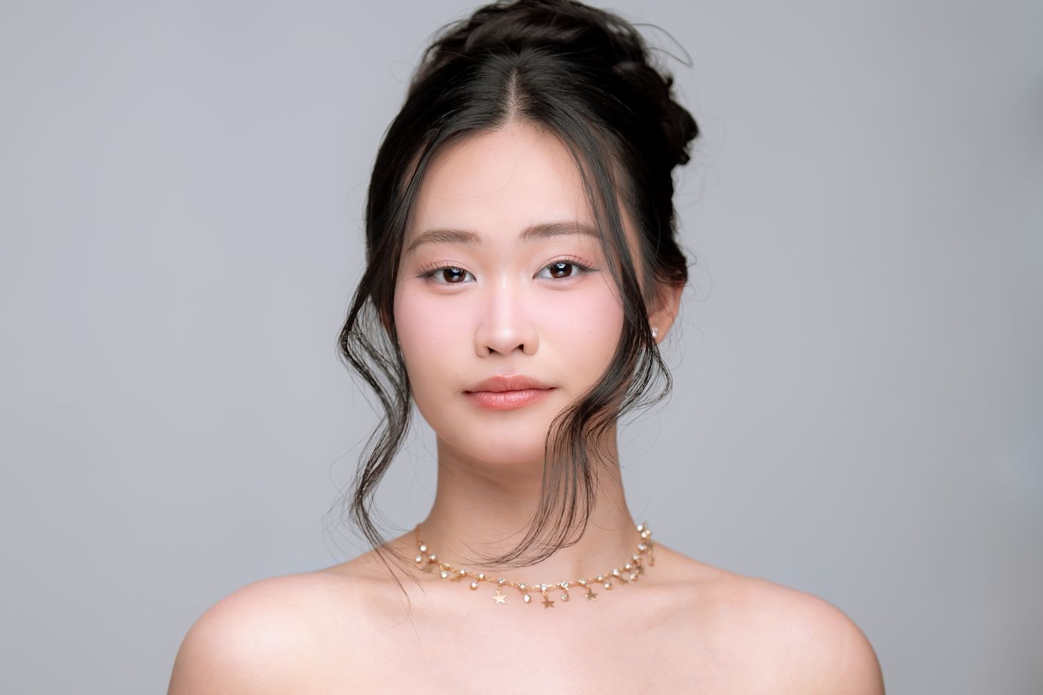 Studio beauty portrait with delicate gold necklace and elegant updo hairstyle.
