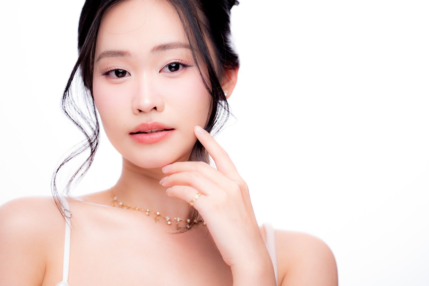 Young Asian woman with elegant updo, gold necklace, and natural makeup poses gracefully against white background.
