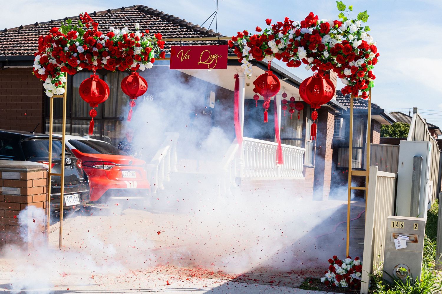 Red floral archway with lanterns and firecrackers smoke during a Chinese wedding celebration outdoors.