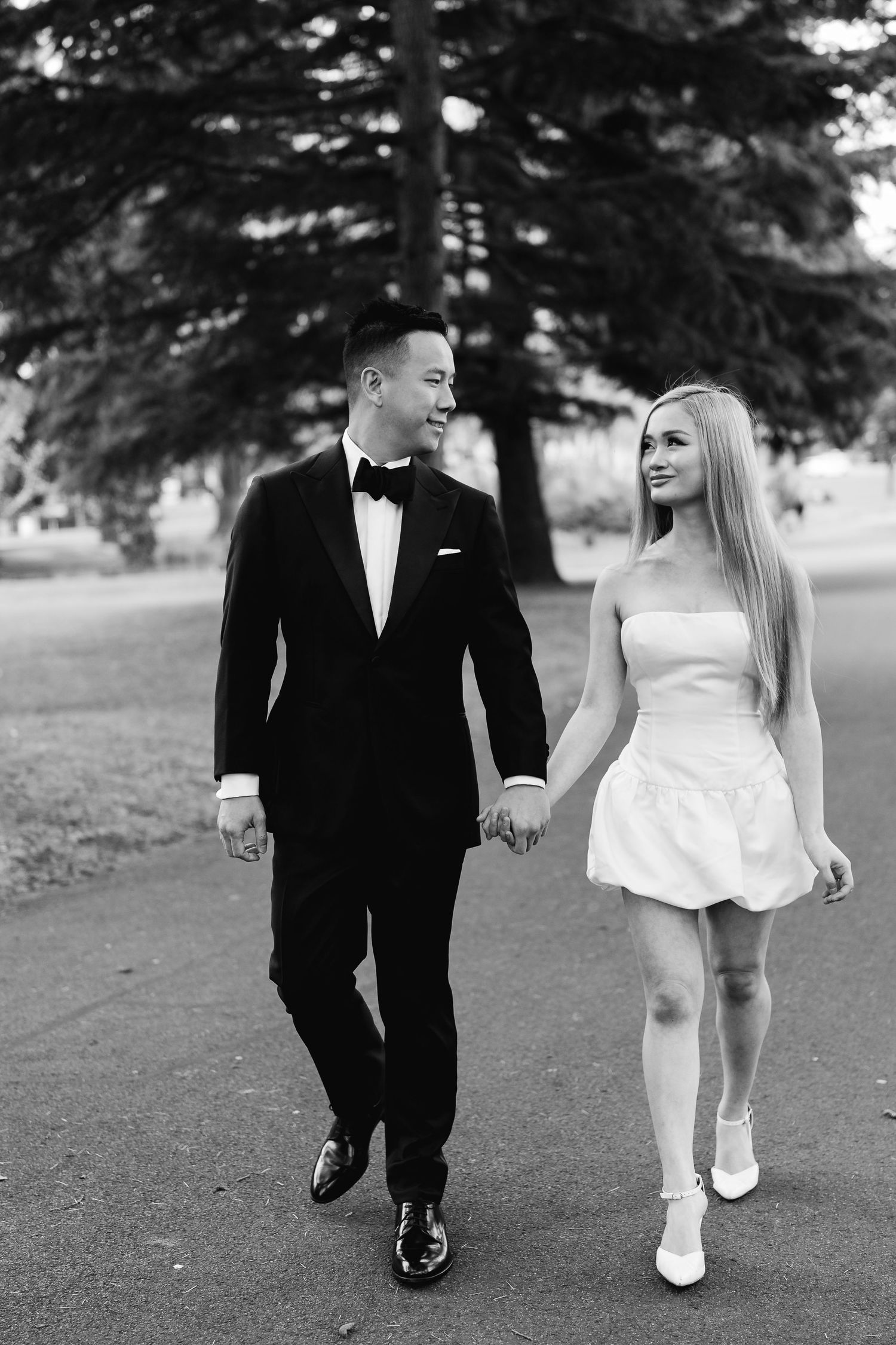 Black and white photo of a couple walking together in formal wedding attire.