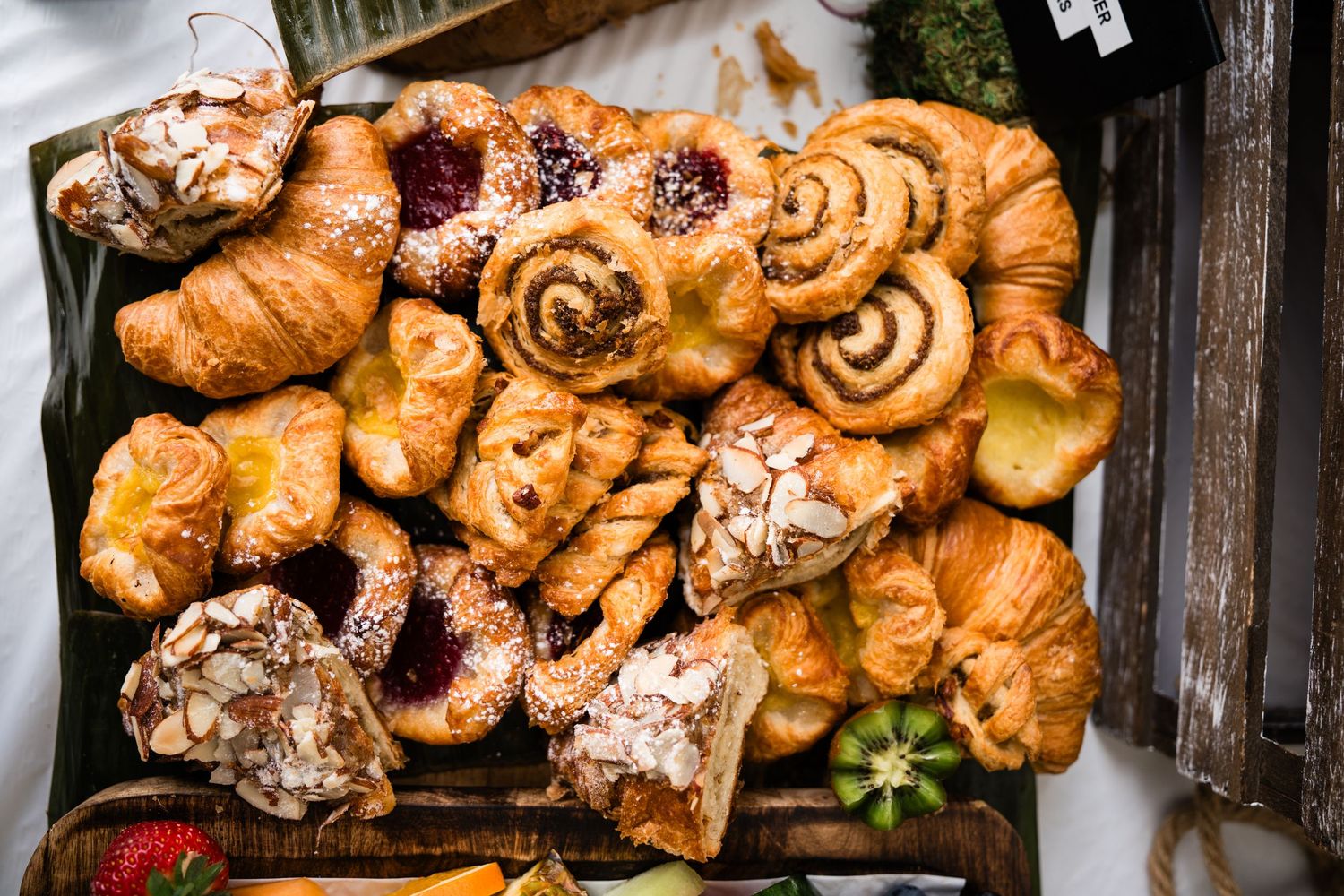 Assorted pastries including croissants, cinnamon rolls, and jam-filled danishes arranged on a wooden tray.