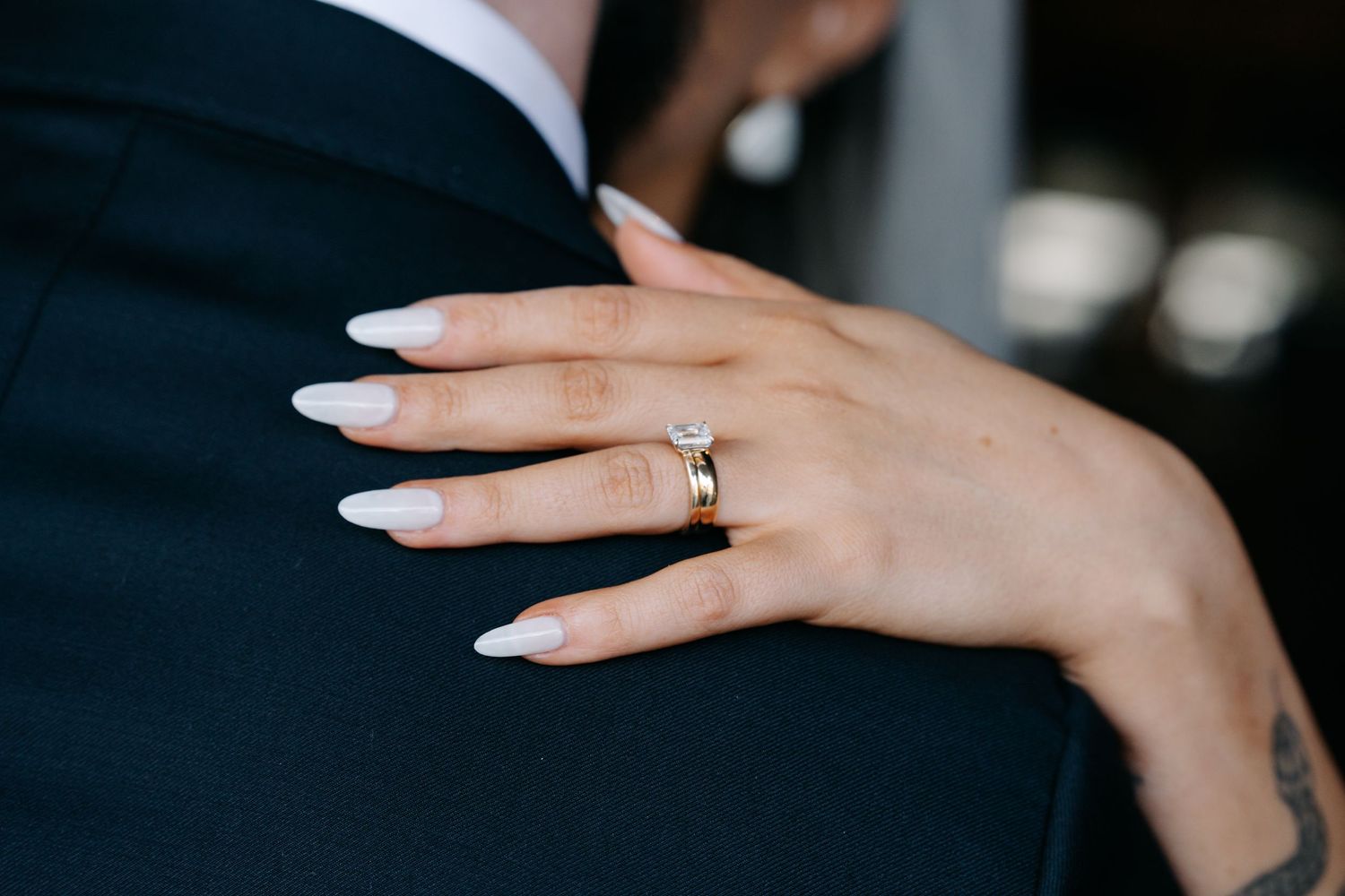 Close-up details of wedding rings and manicured hands against dark background.