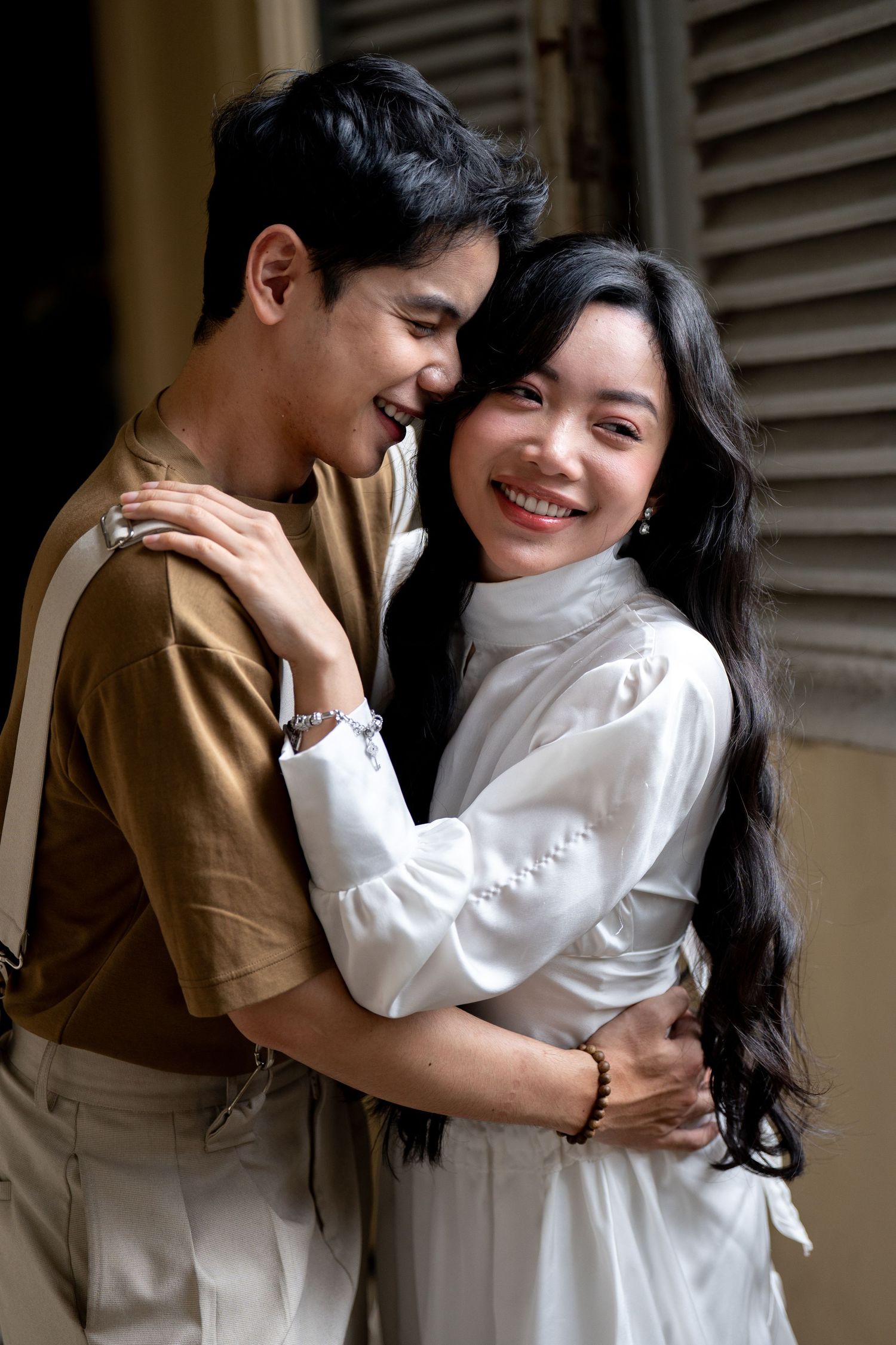 A couple embraces tenderly while wearing coordinated brown and white outfits indoors.