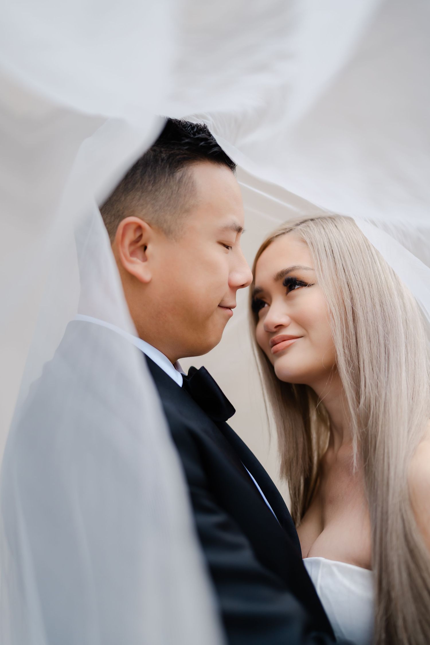 Intimate wedding portrait captured through flowing white veil showing tender romantic moment.
