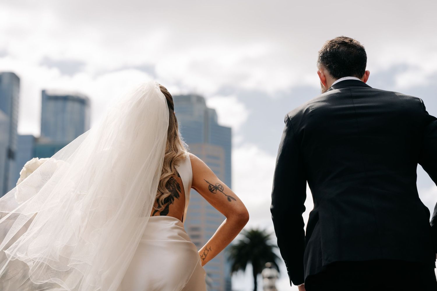 Wedding couple overlooking city skyline with bride's veil flowing in the wind.
